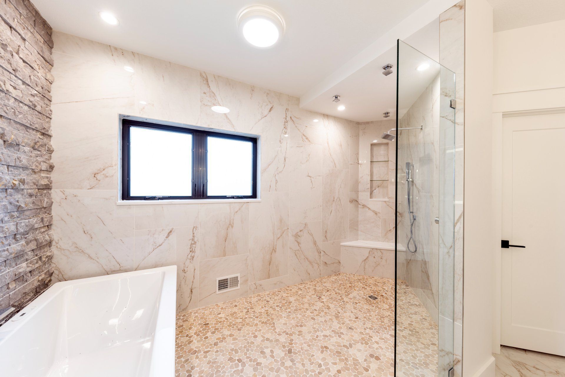 Modern bathroom with stone tile walls, glass shower, and soaking tub.
