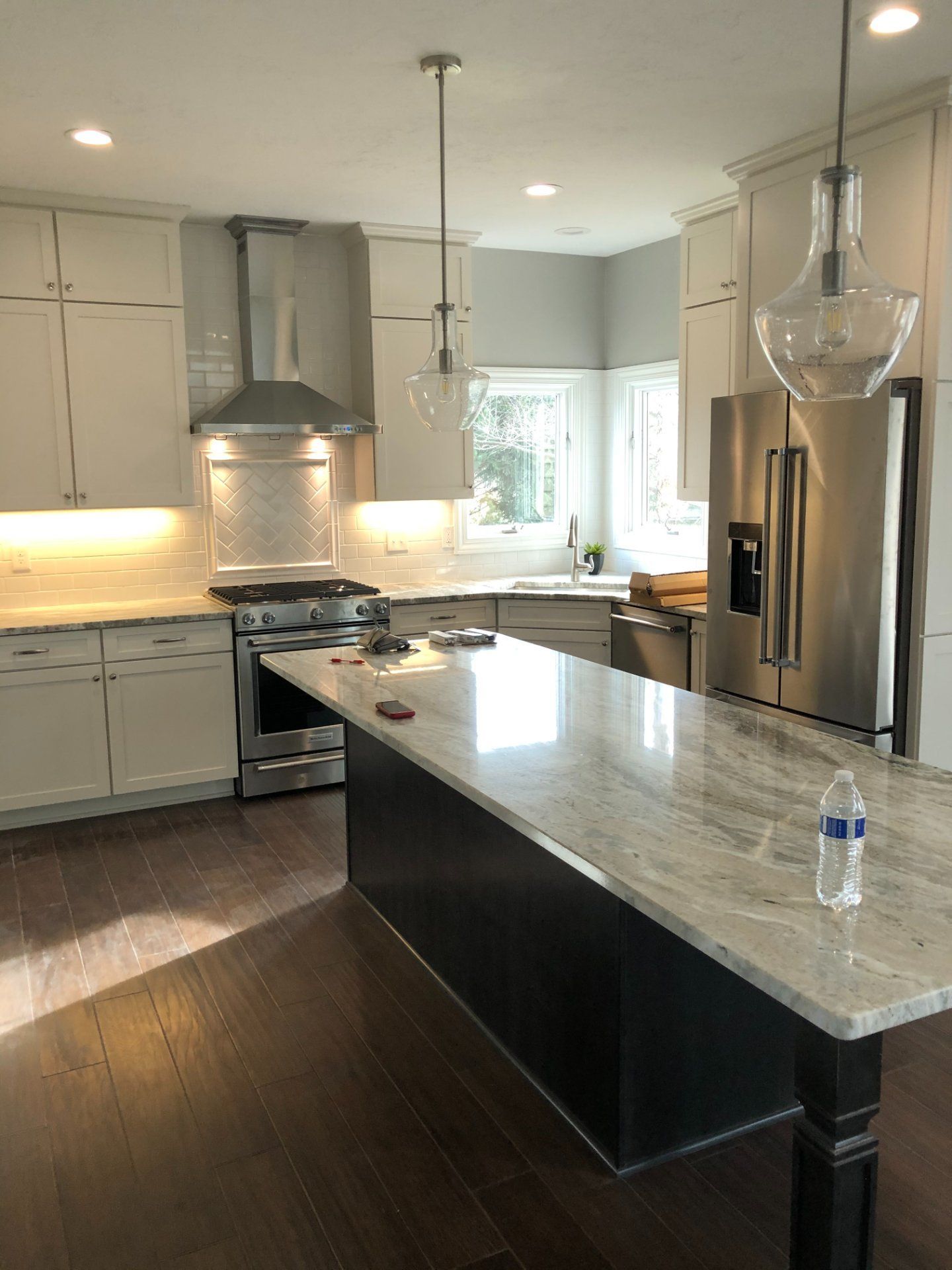 Modern kitchen with white cabinets, stainless steel appliances, dark island, and wood floors.