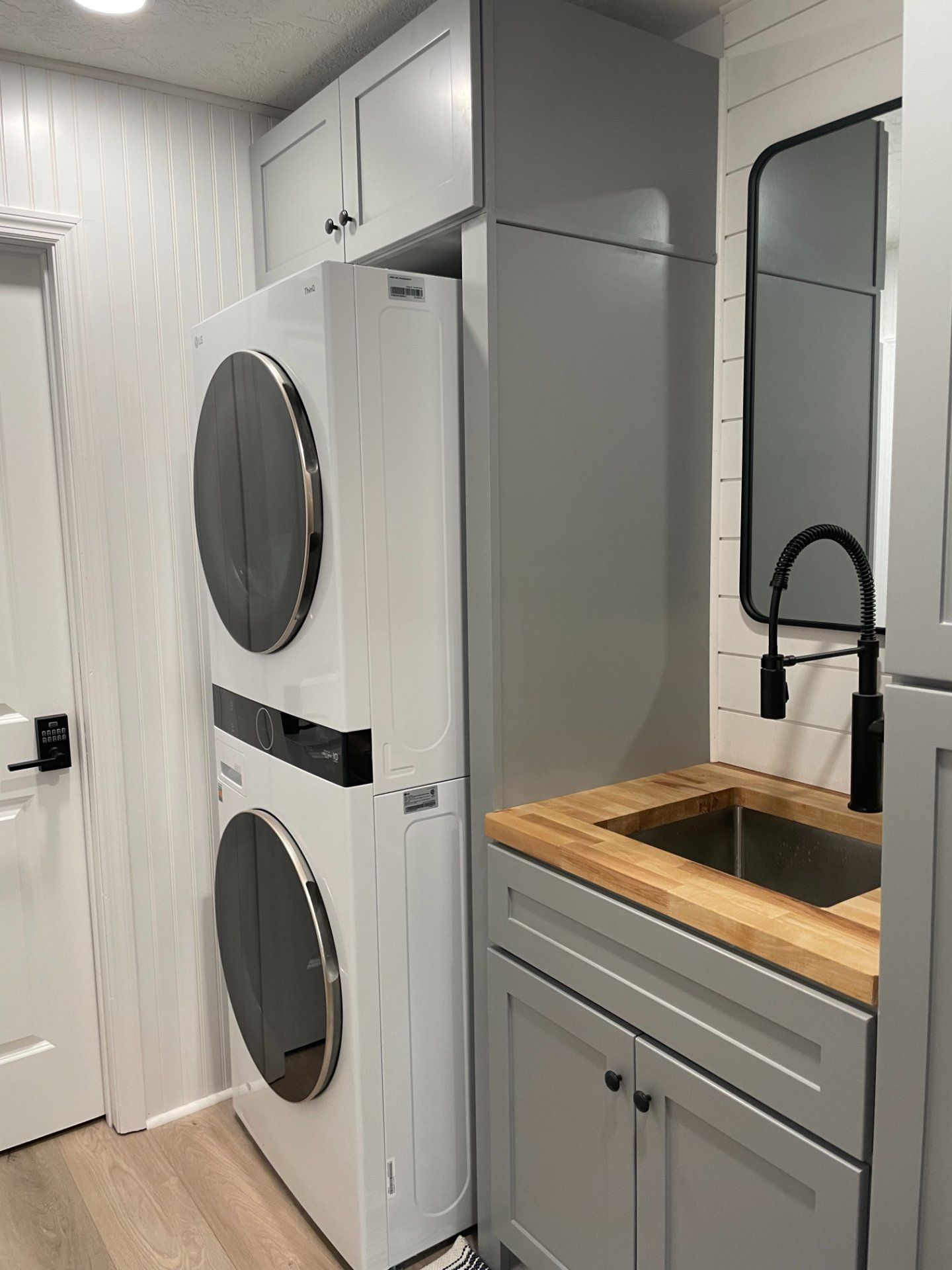 Stacked washer and dryer unit next to a gray cabinet with a sink and wood countertop.