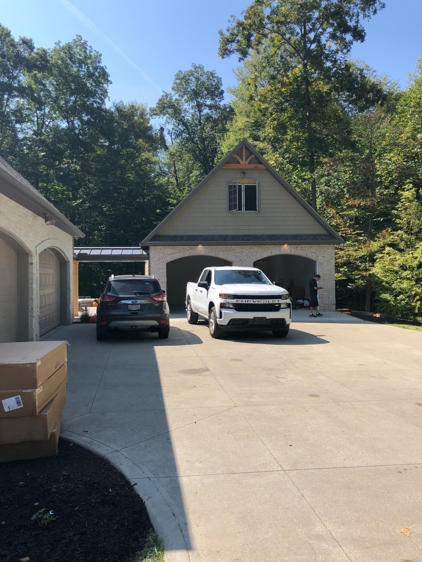 SUV and pickup truck parked in front of a tan garage with attached carport, surrounded by trees.