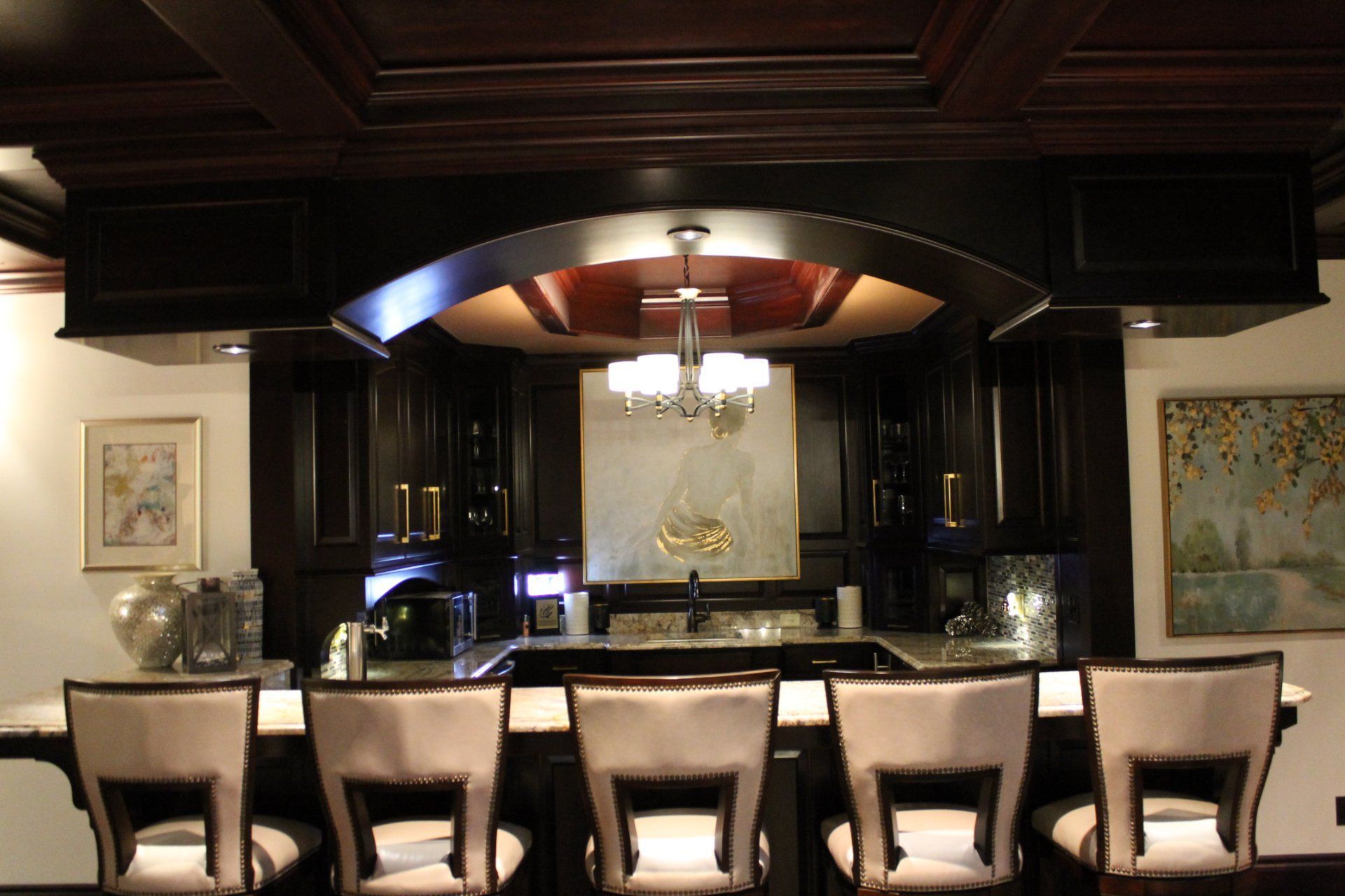 Dark wood home bar with countertop, stools, and chandelier.