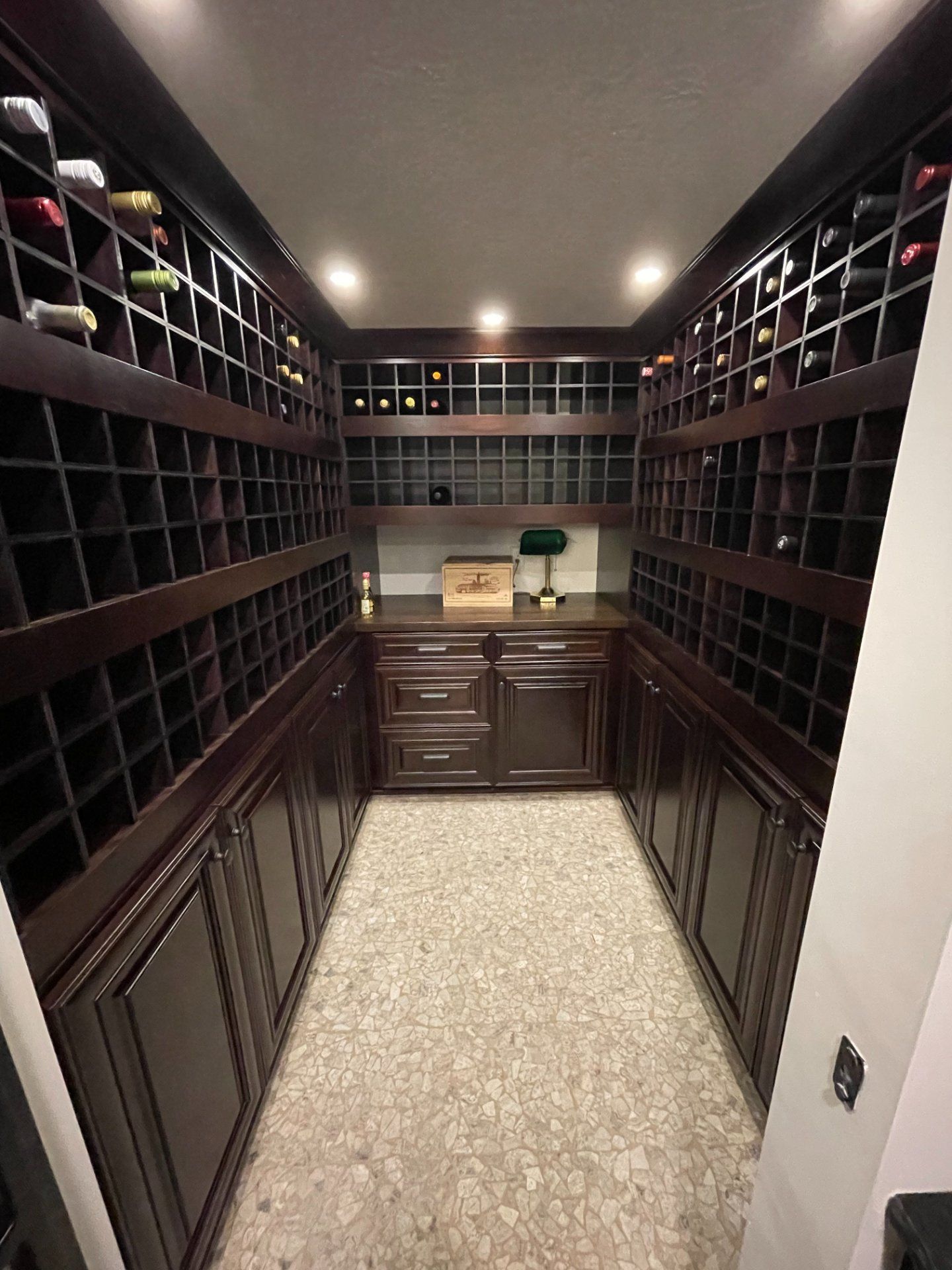 Wine cellar with dark wooden racks and cabinets, bottles stored, with central counter.