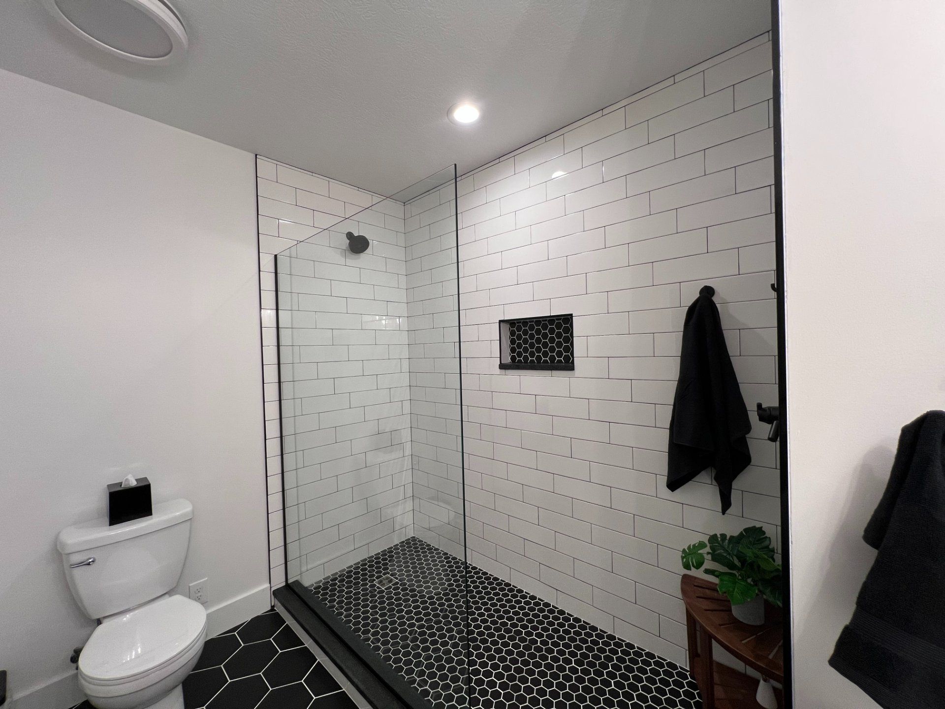 Modern bathroom with black and white tile shower and toilet. Black towel hanging.