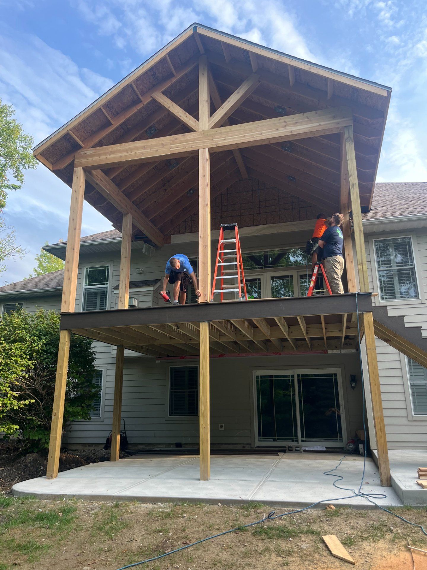 Construction of a new wooden deck and roof addition on a house; workers building outdoors.