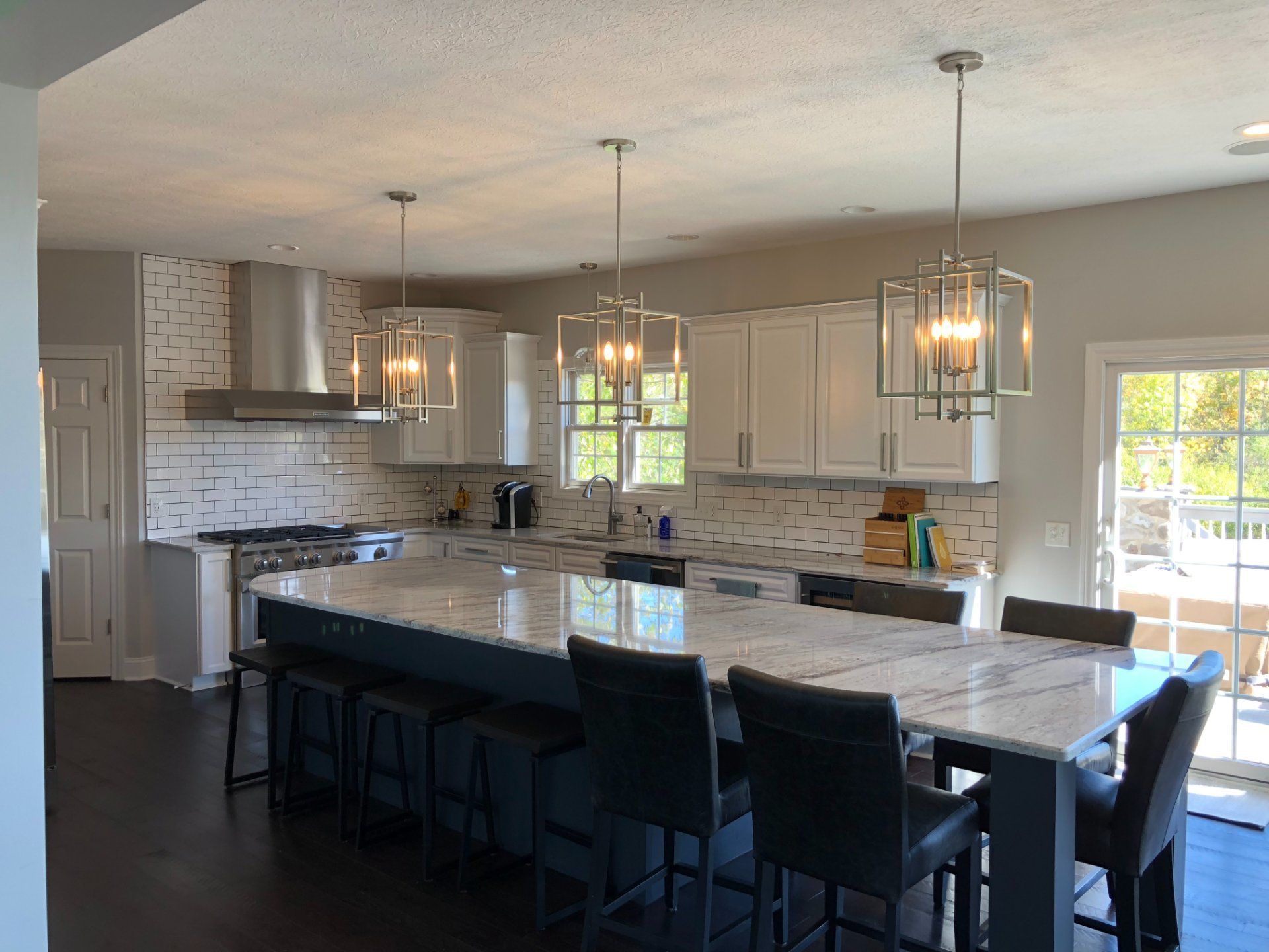 Modern kitchen with white cabinets, dark blue island, granite countertops, and pendant lights.