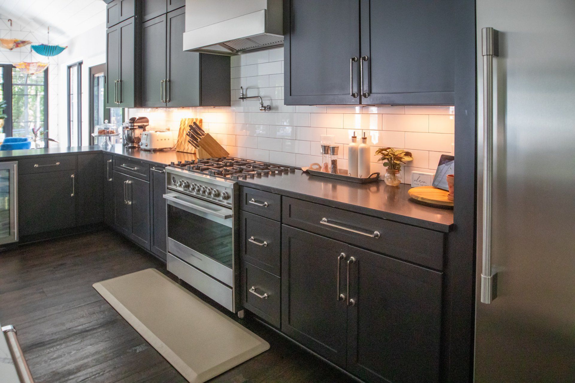Dark kitchen with black cabinets, stainless steel appliances, and white tiled backsplash.