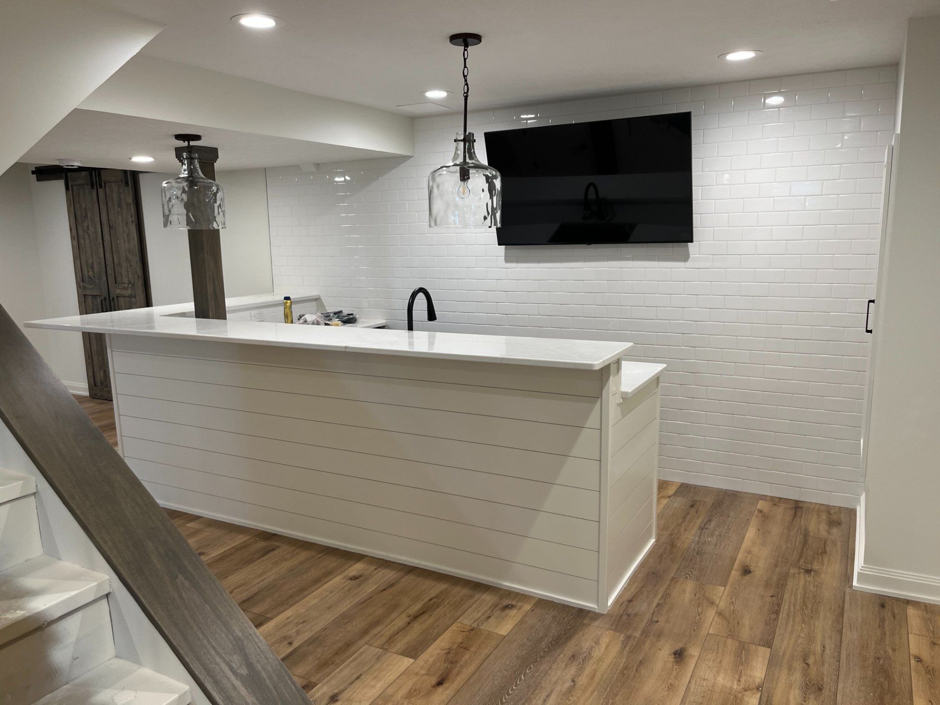Finished basement with a bar, TV, white brick wall, and wood-look flooring.