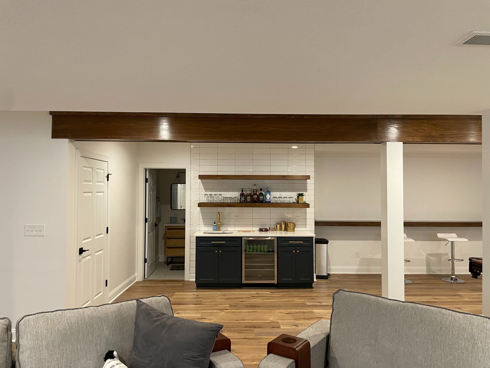 Living room with bar and hardwood floor; dark cabinets, brown beam and white walls.