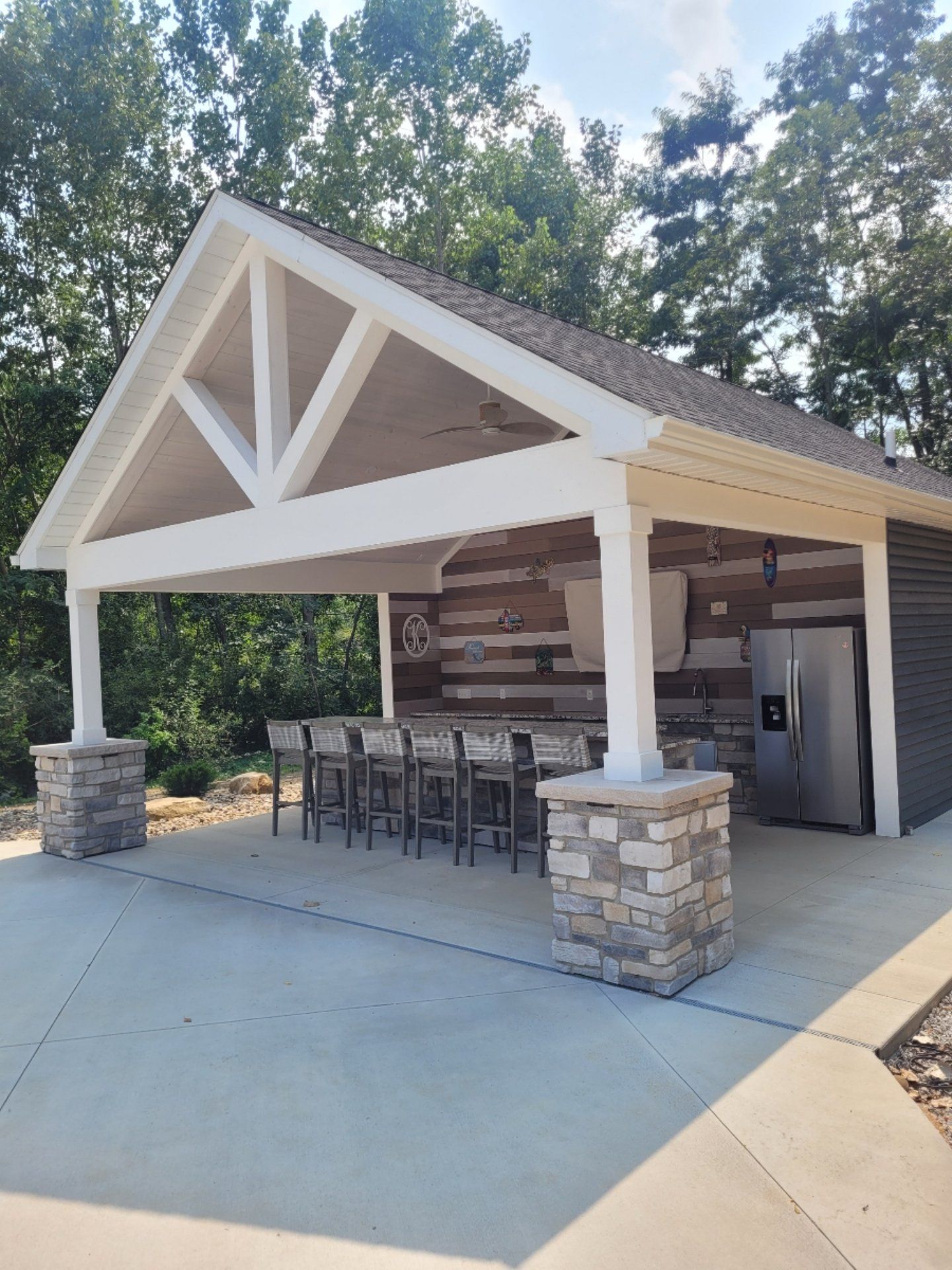 Outdoor pavilion with a bar area, stone pillars, and wooden accents; surrounded by trees.