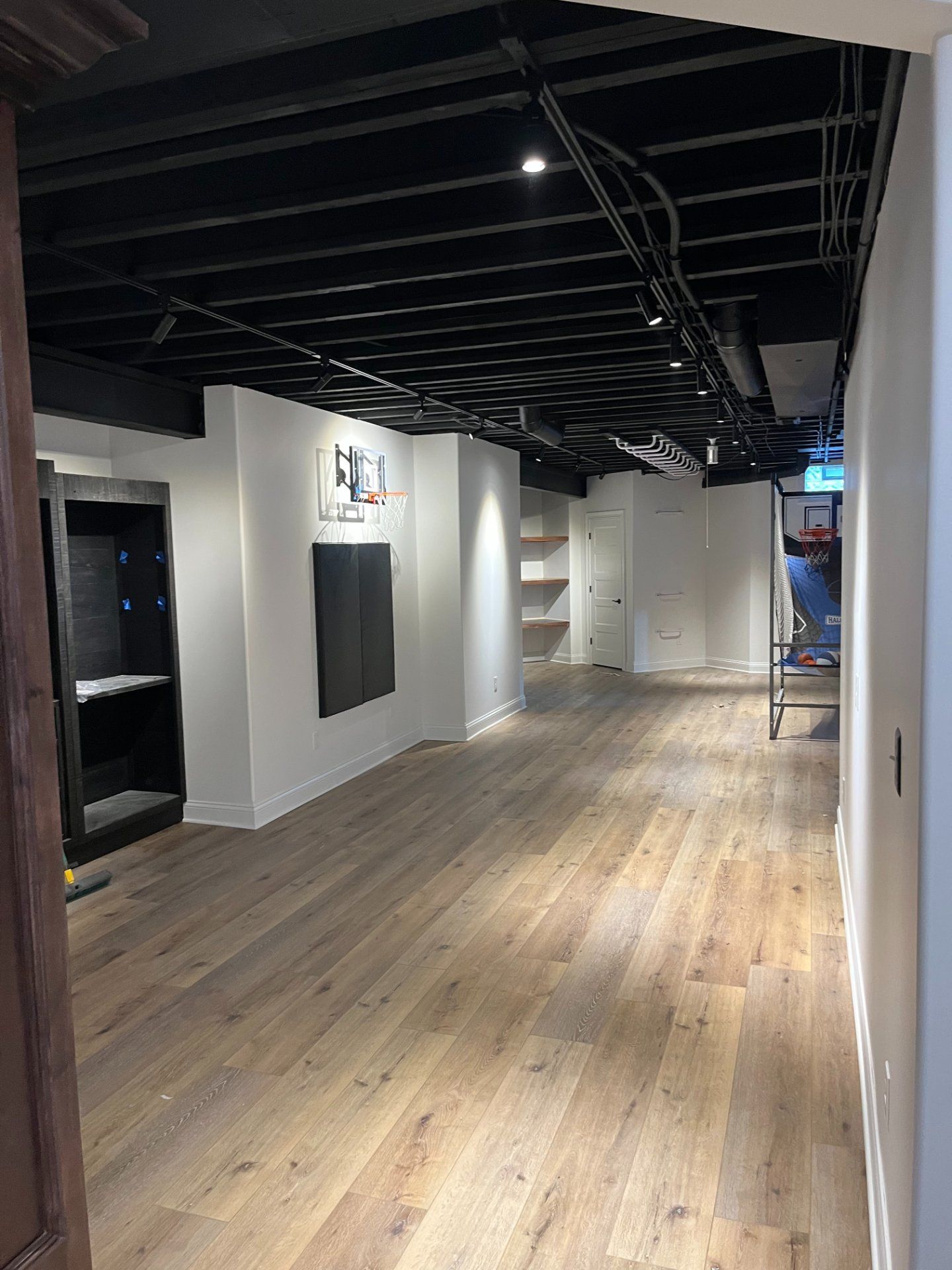 Finished basement with wood flooring, white walls, black ceiling, and built-in shelving.