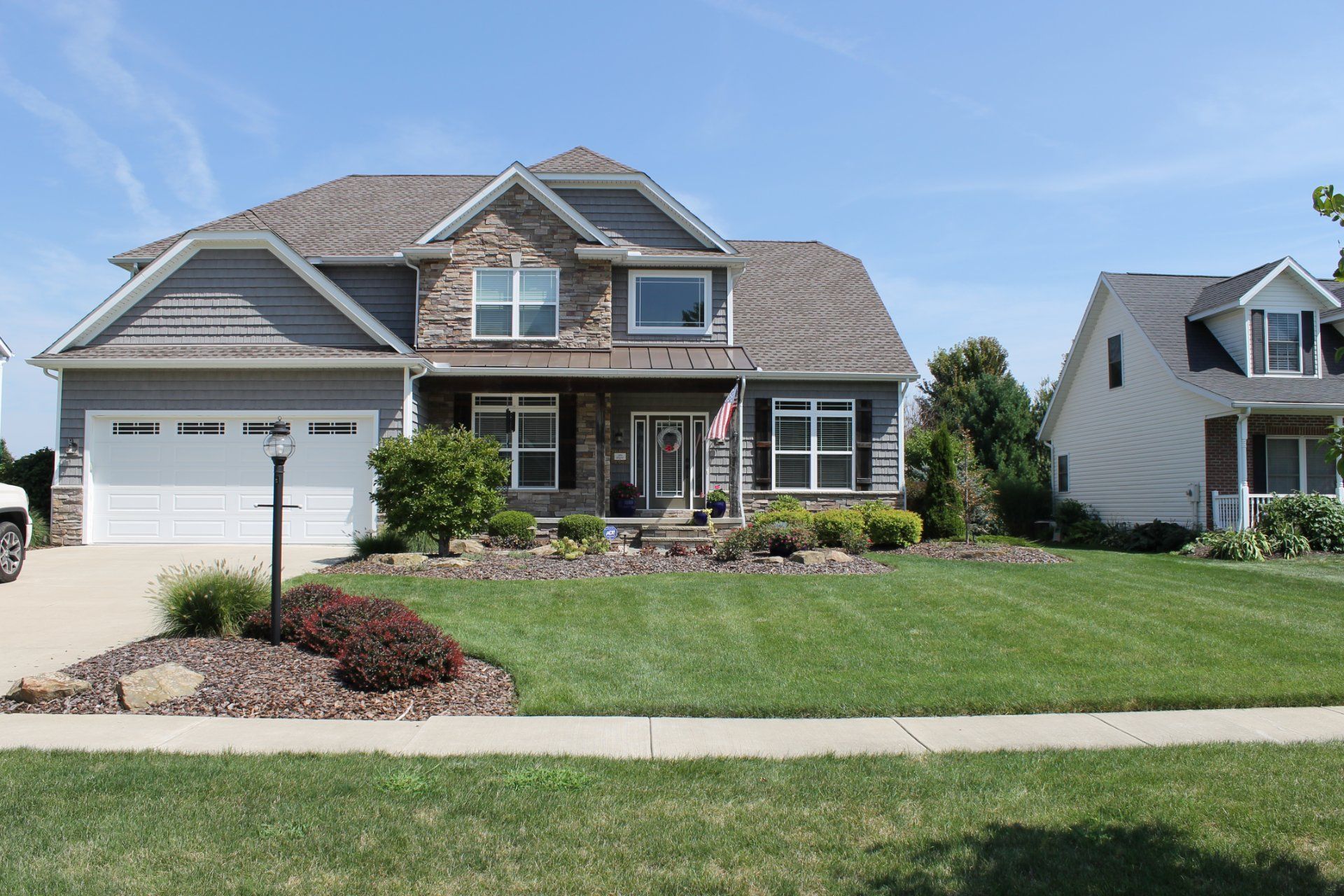 Two-story house with gray siding, stone accents, and a well-manicured lawn on a sunny day.