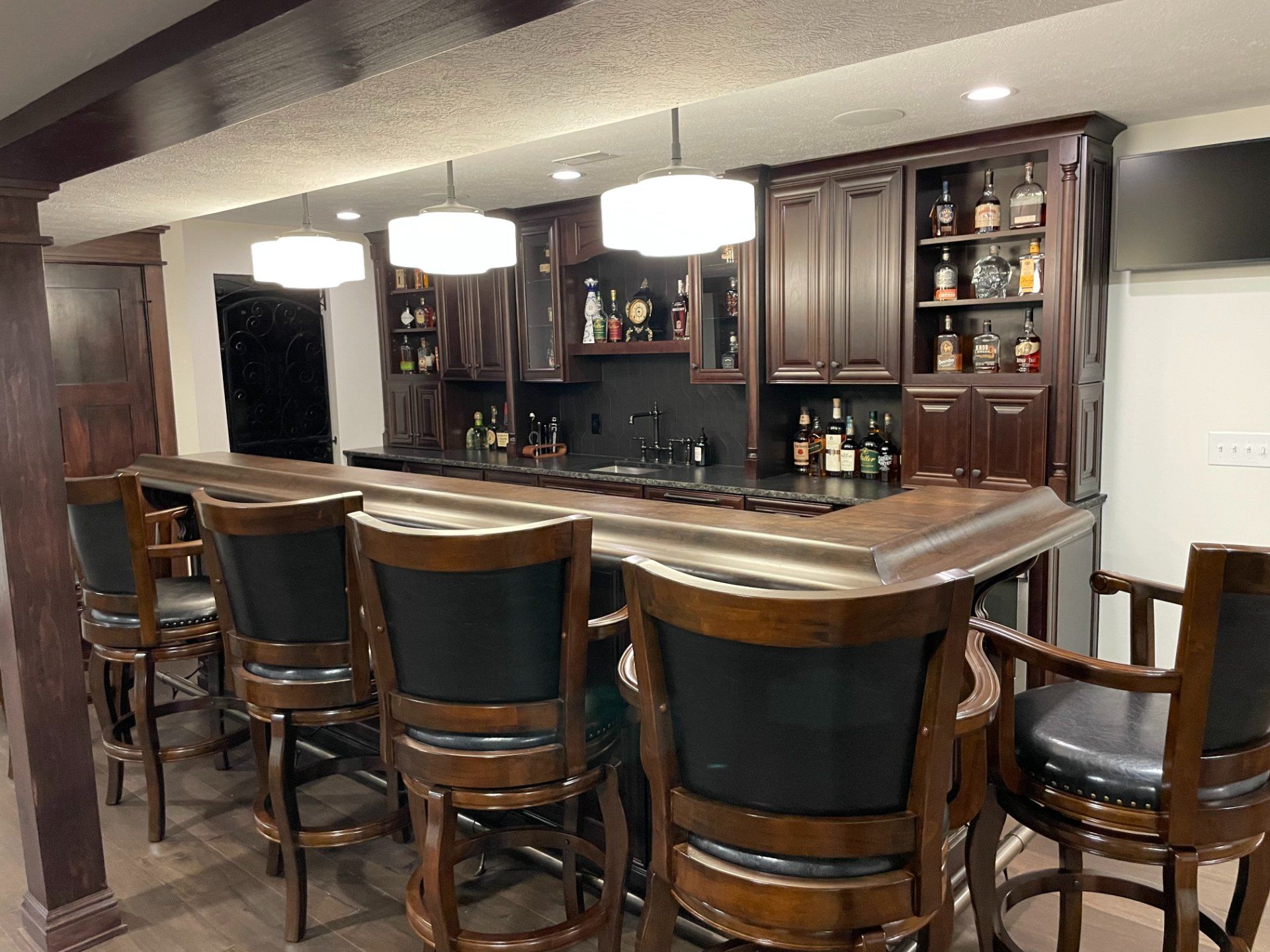 Interior bar with seating and liquor display. Brown cabinets, bar stools, and countertops. Overhead lights.