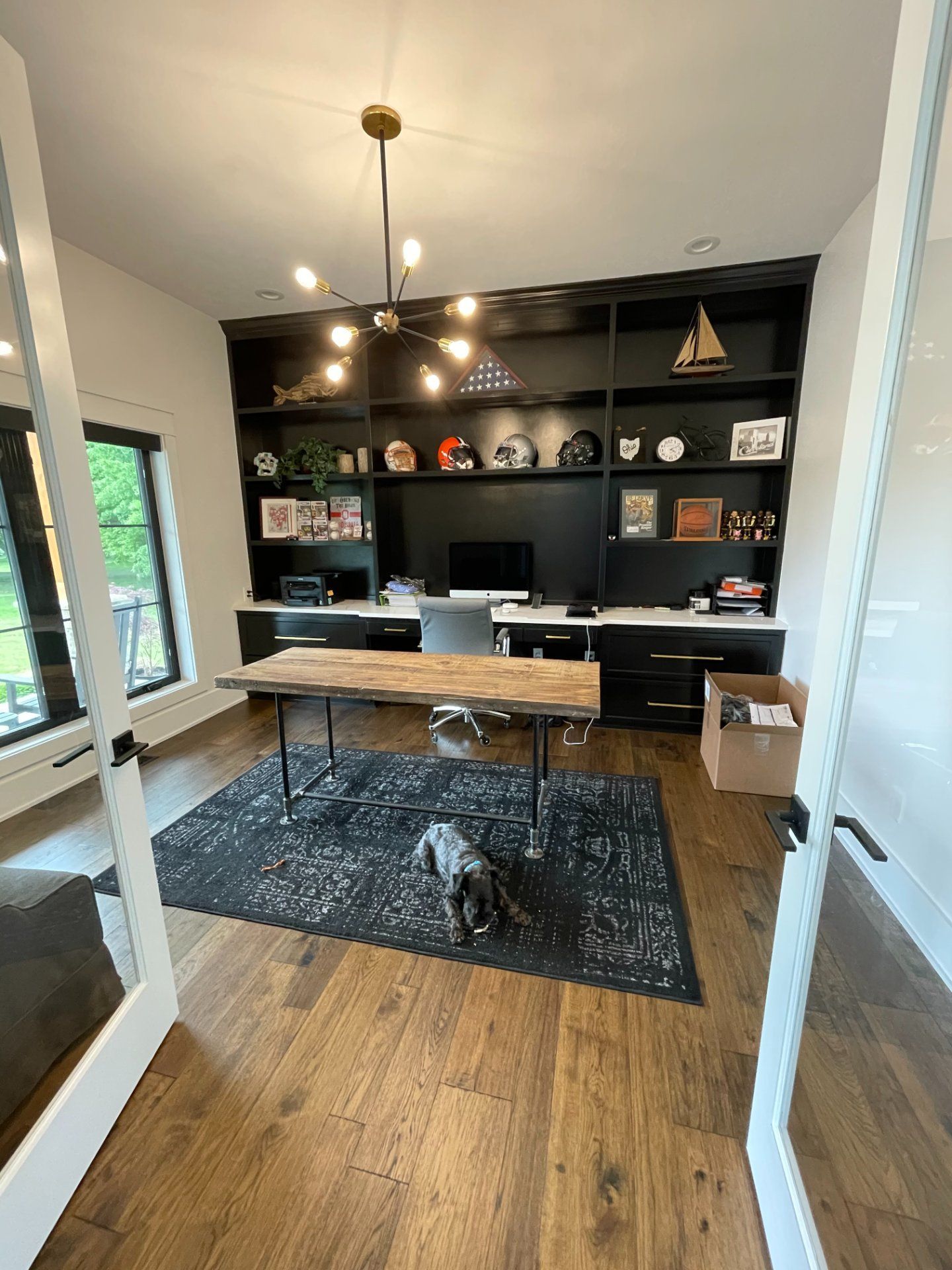 Home office with black built-in shelving, desk, dark rug, and hardwood floors.