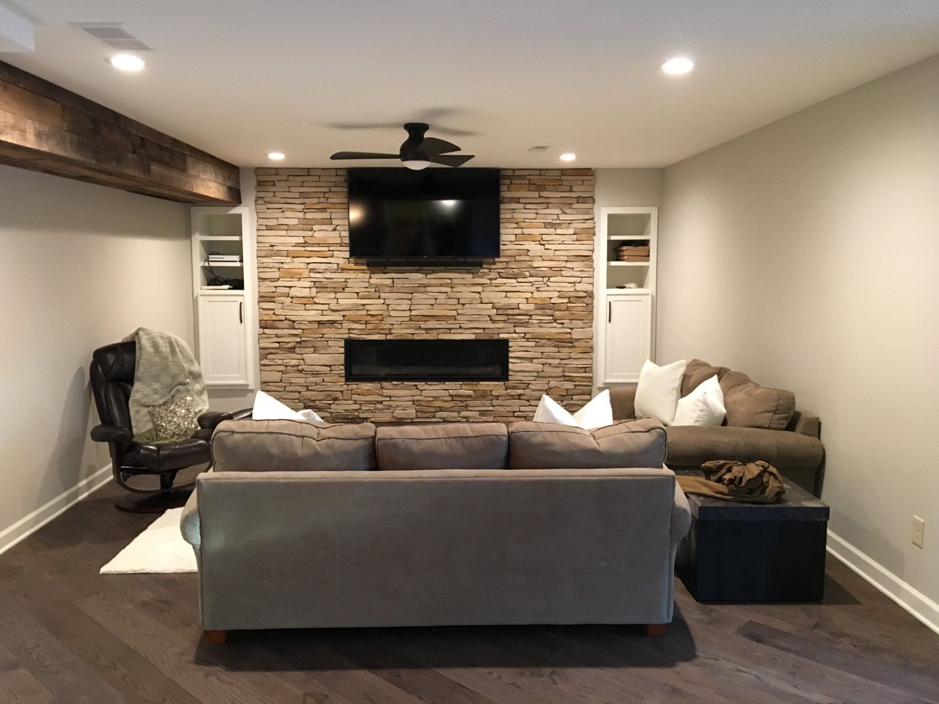 Living room with stone fireplace, built-in shelves, TV, and couches. Dark wood floors.