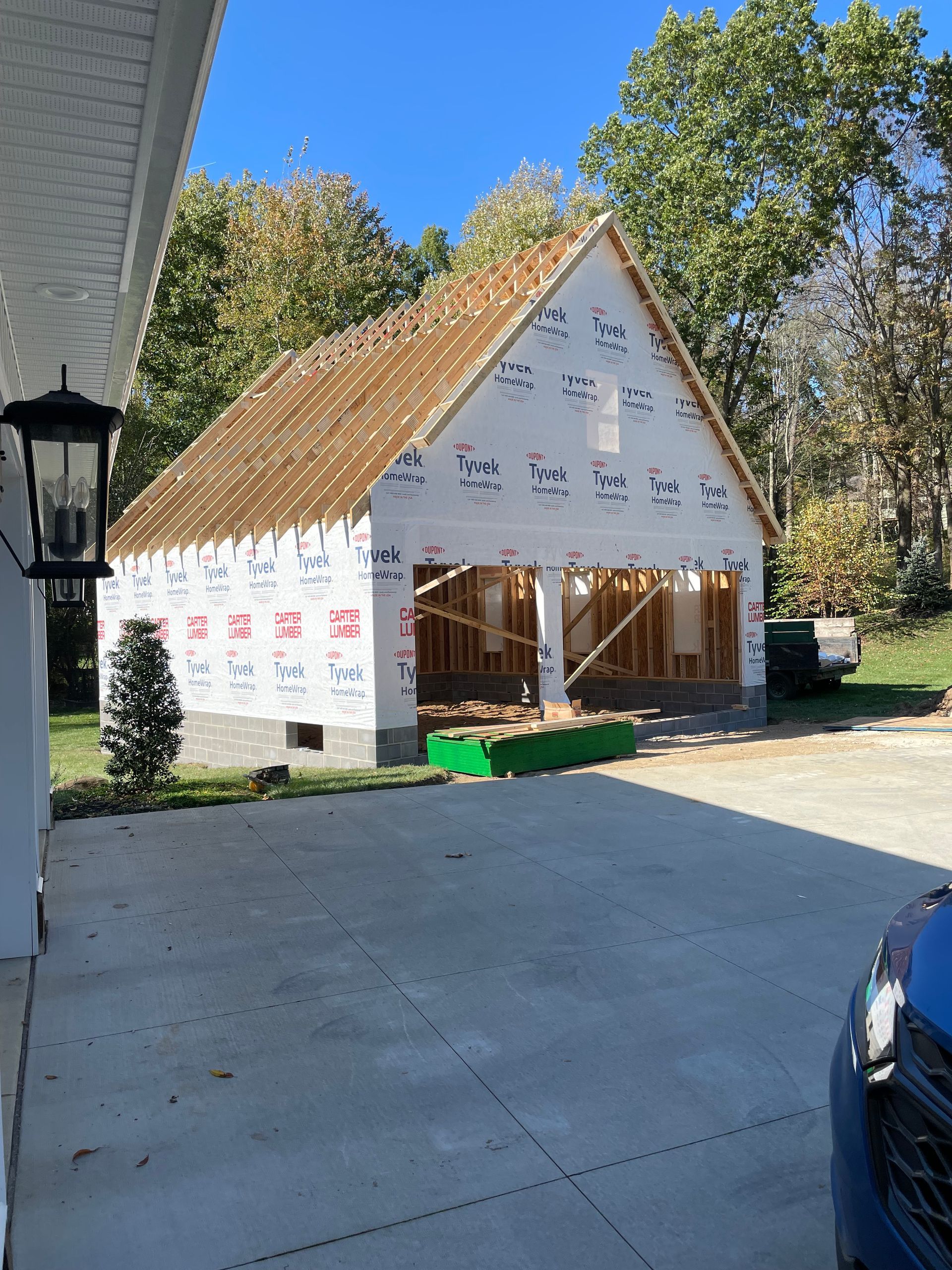 Garage under construction with white sheathing and exposed framing, brown roof, and concrete driveway.