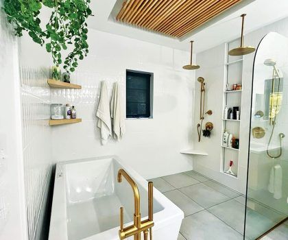 Modern white bathroom with gold fixtures, a soaking tub, shower, and wooden ceiling detail.