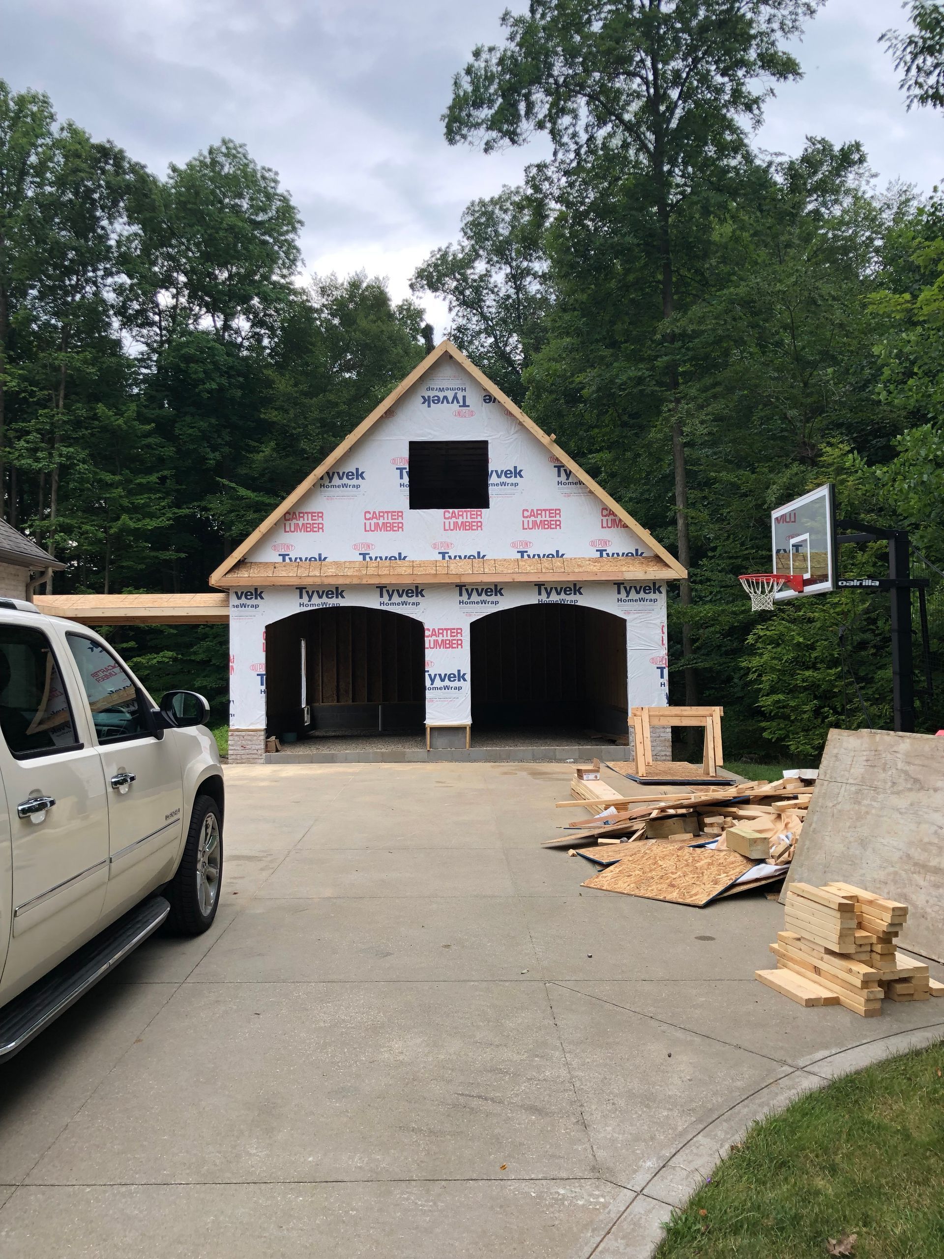 Two-car garage under construction with a white truck parked in the driveway. A basketball hoop is beside it.