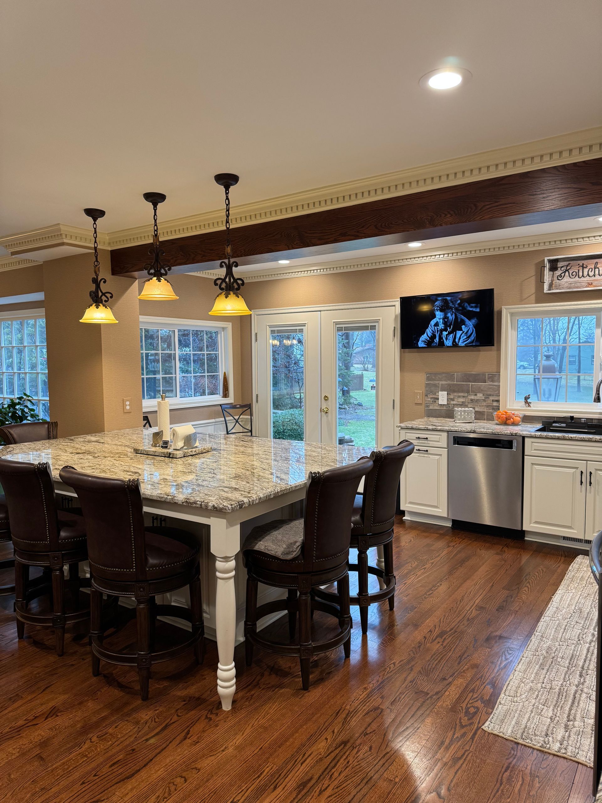 Kitchen with large island, pendant lights, French doors, granite countertops, and wood floors.