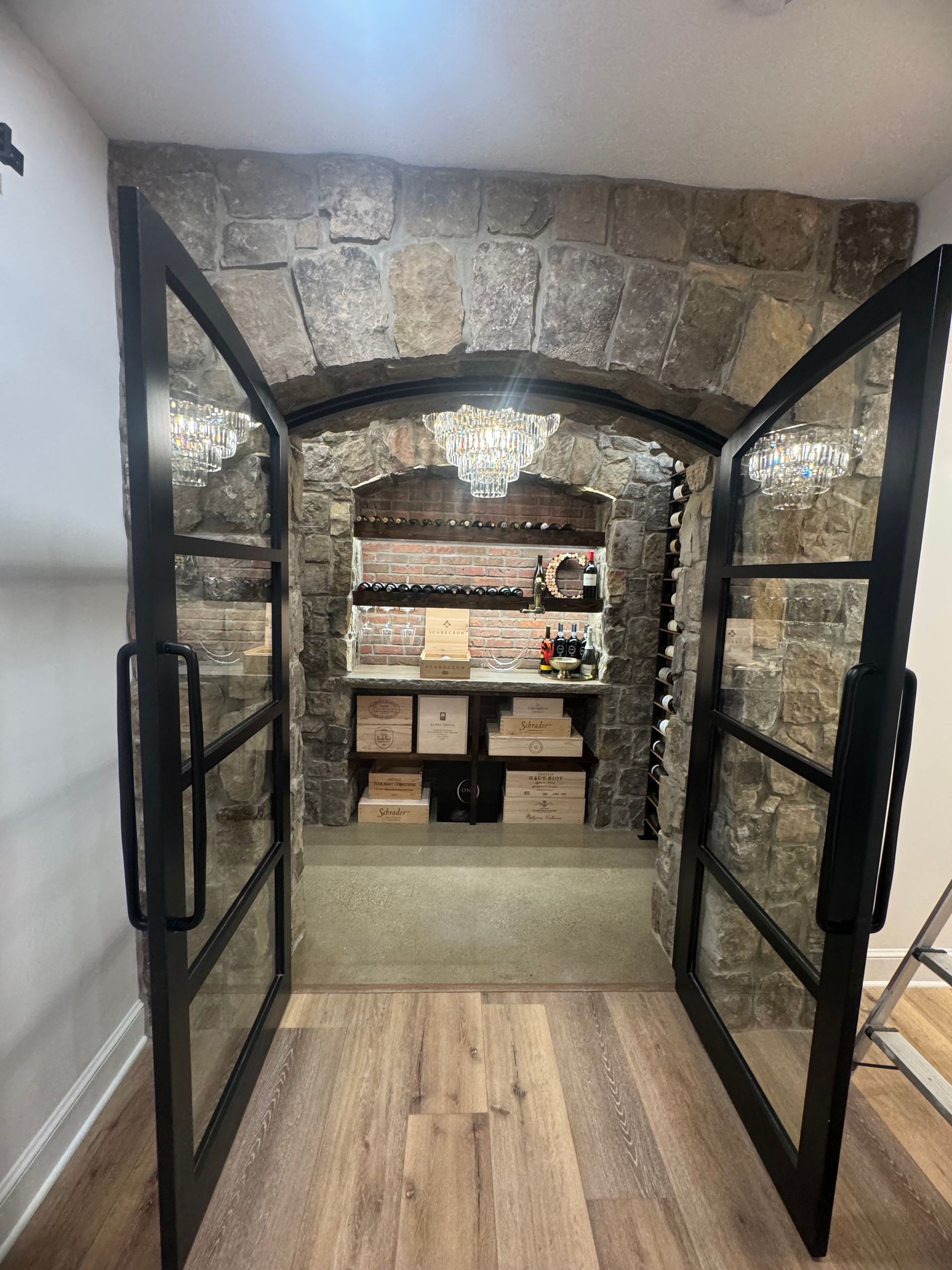Wine cellar entrance with stone archway, glass doors, and wooden flooring.
