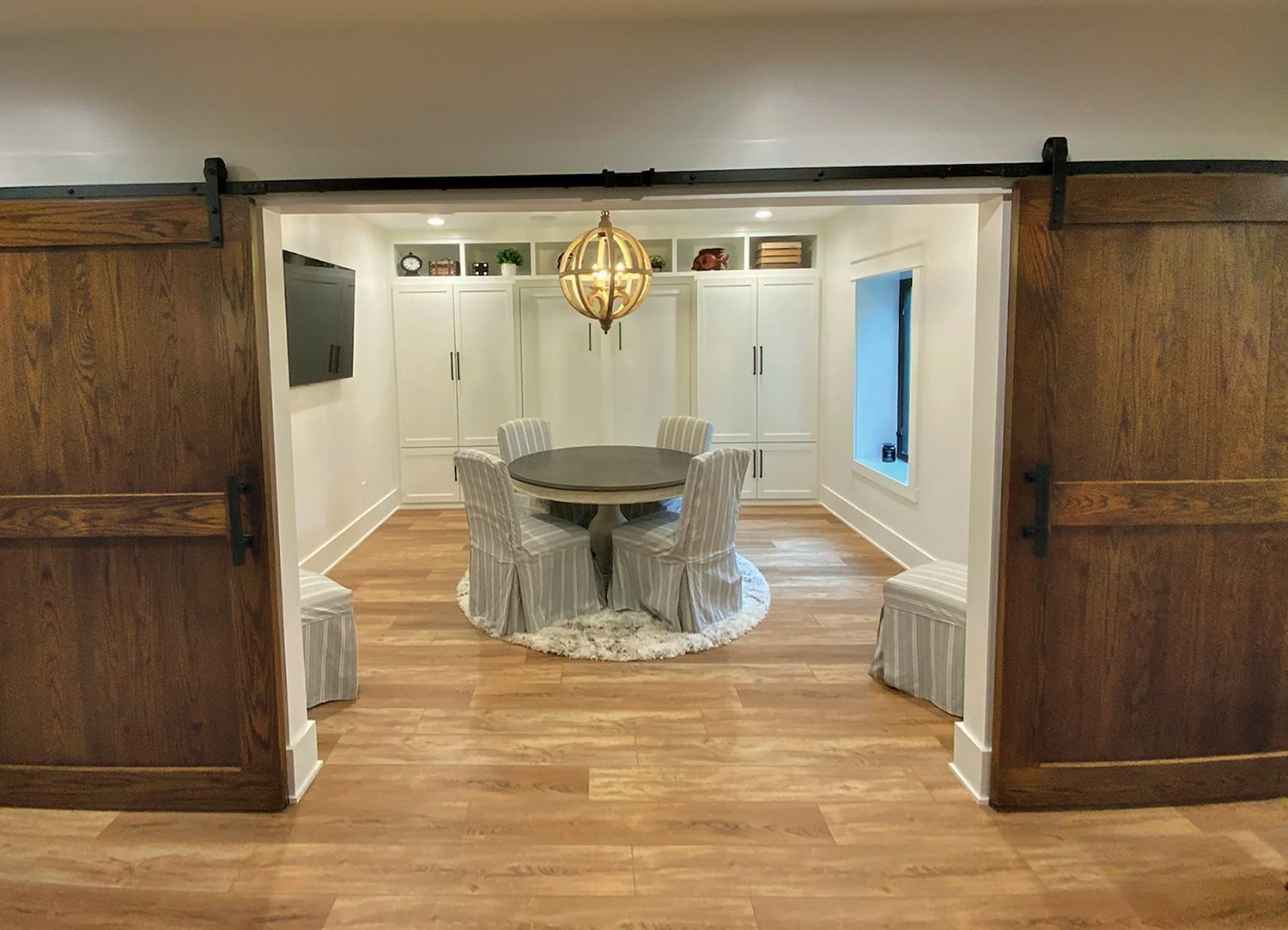 Barn doors open to a dining area: round table, chairs, decorative light fixture, built-in shelves and cabinets.