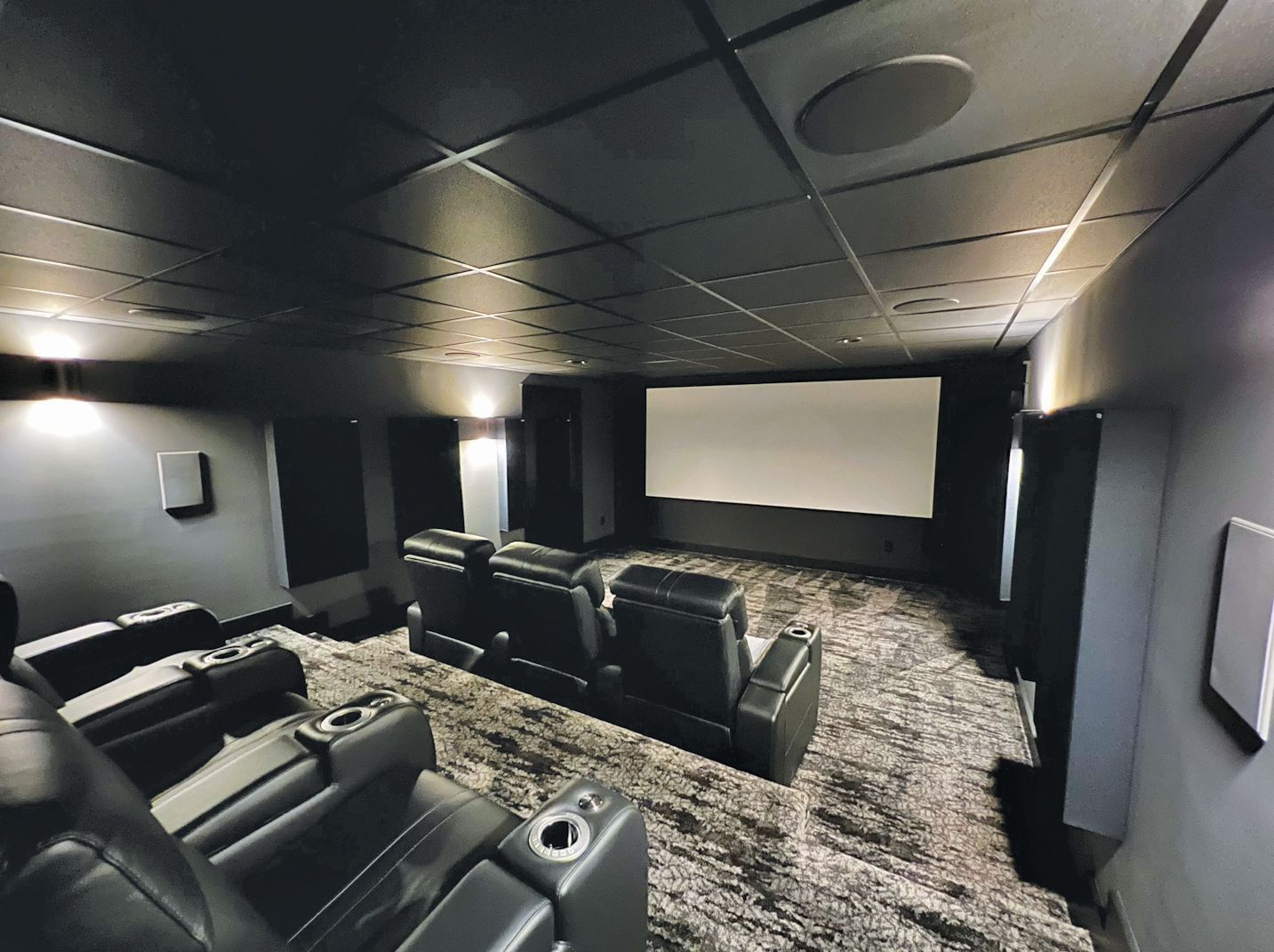 Home theater with black ceiling, walls, seats, screen, and speakers. Carpeting.