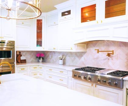 Elegant white kitchen with marble countertops, gold hardware, and a stainless steel stove.