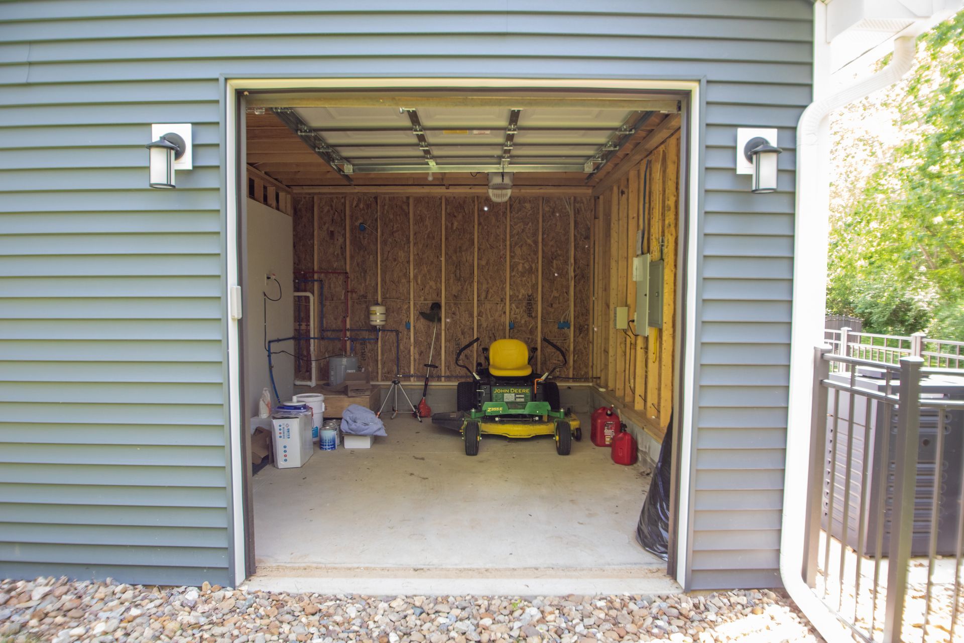 Open garage with green siding. Lawn mower inside, along with other items.