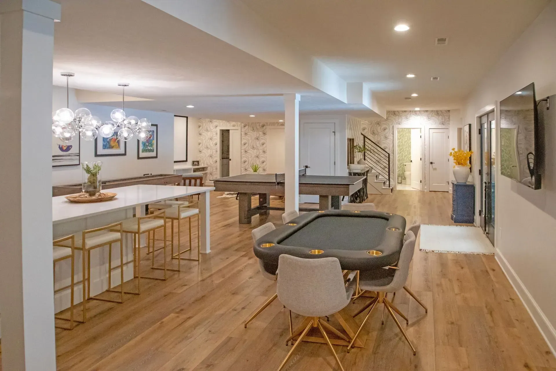 Spacious game room with a poker table, pool table, bar, and seating; hardwood floors, white walls.
