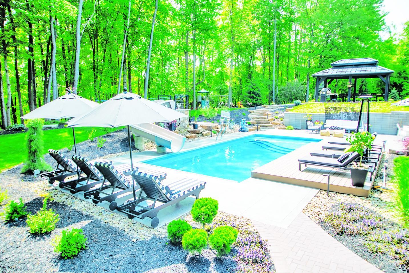 Swimming pool with lounge chairs, umbrellas, gazebo, surrounded by trees.