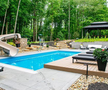 Swimming pool with slide, lounge chairs, and gazebo, surrounded by trees.