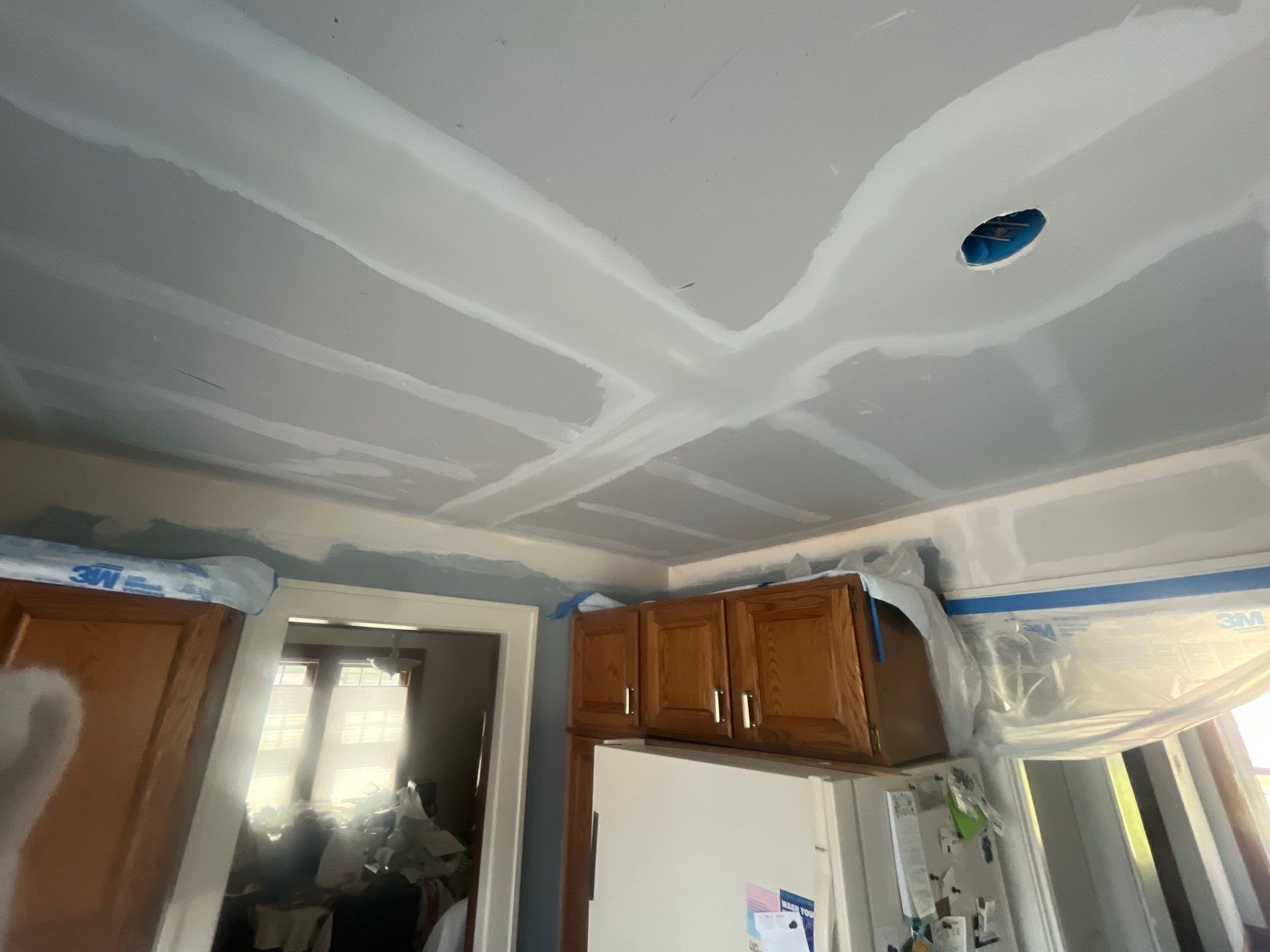 A kitchen with wooden cabinets and a ceiling that is being painted.