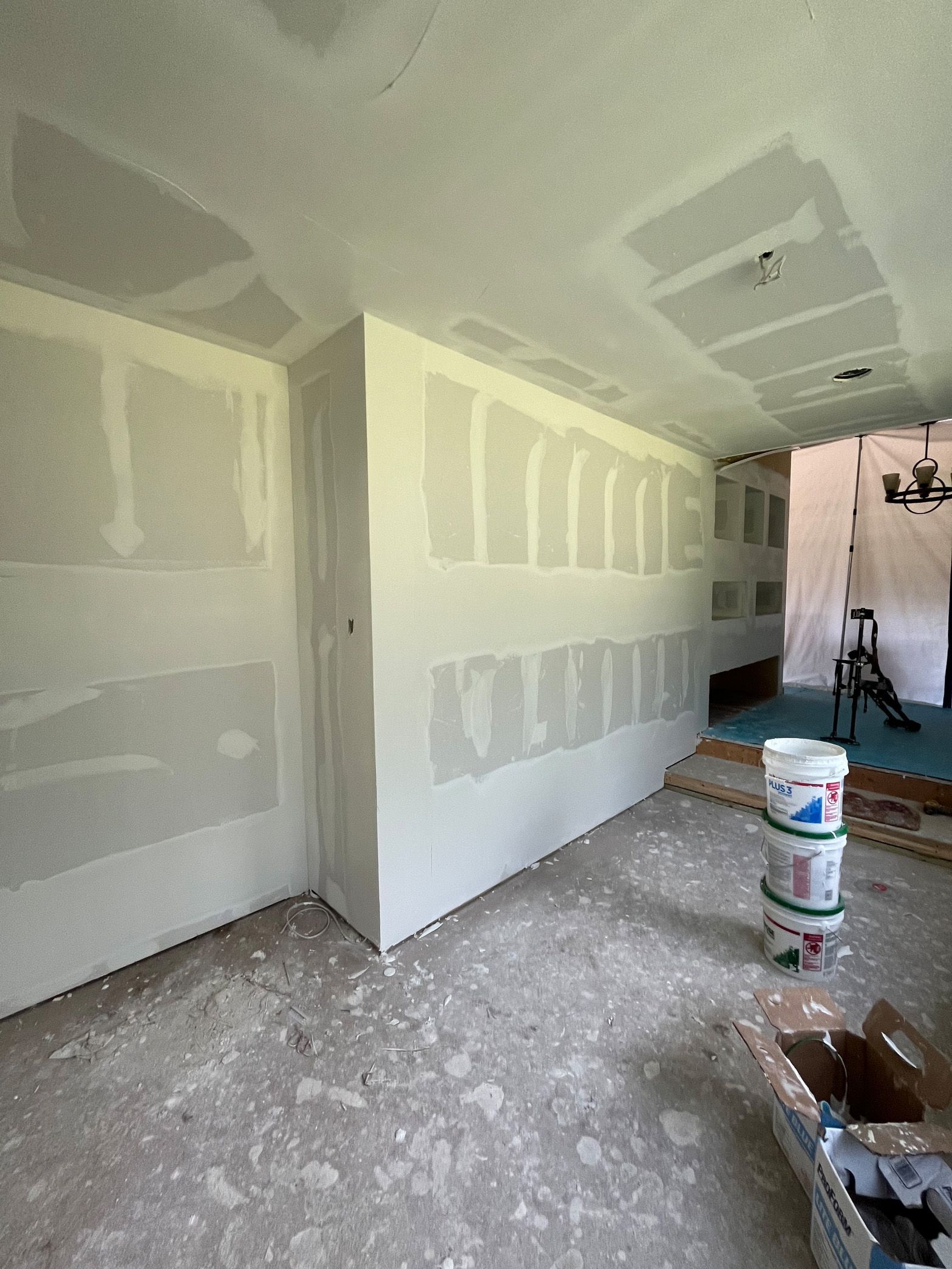 A room with drywall on the walls and a bucket of paint on the floor.