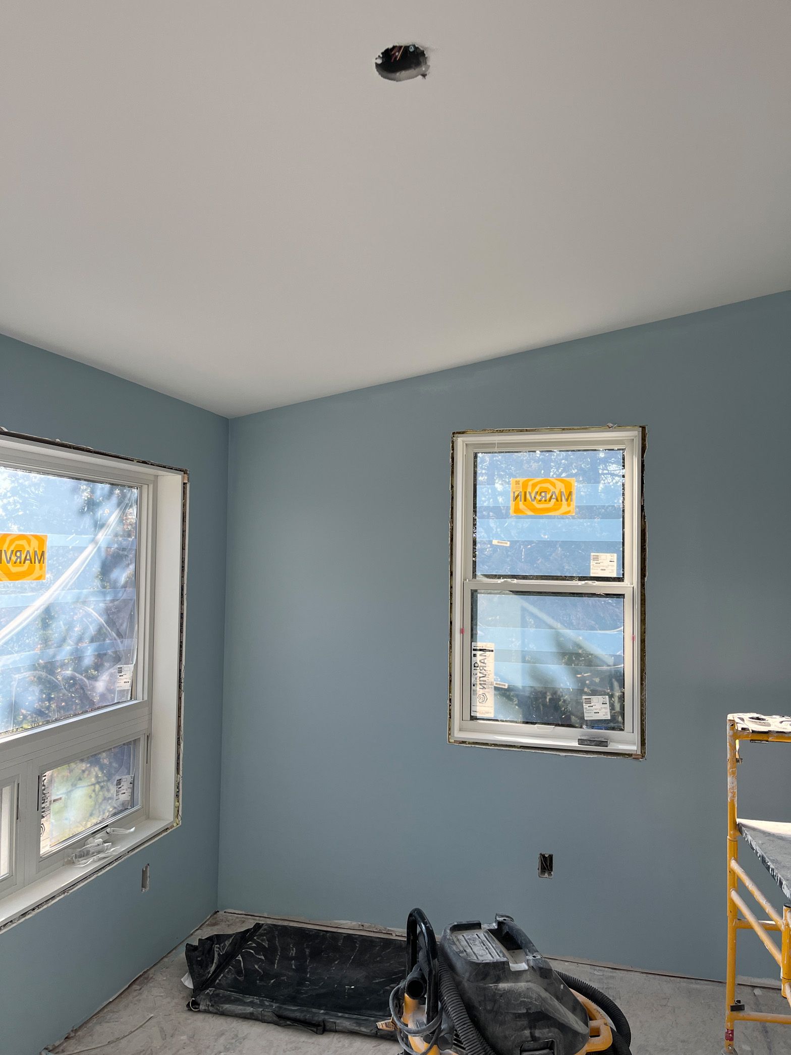 A room with blue walls and two windows under construction.