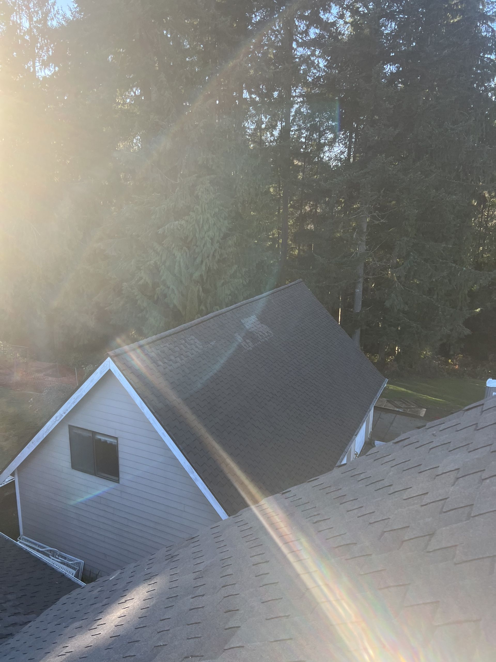 Sunlight over a house with a dark roof and a smaller building beside it by Team Roofing NW in Bonney Lake, WA