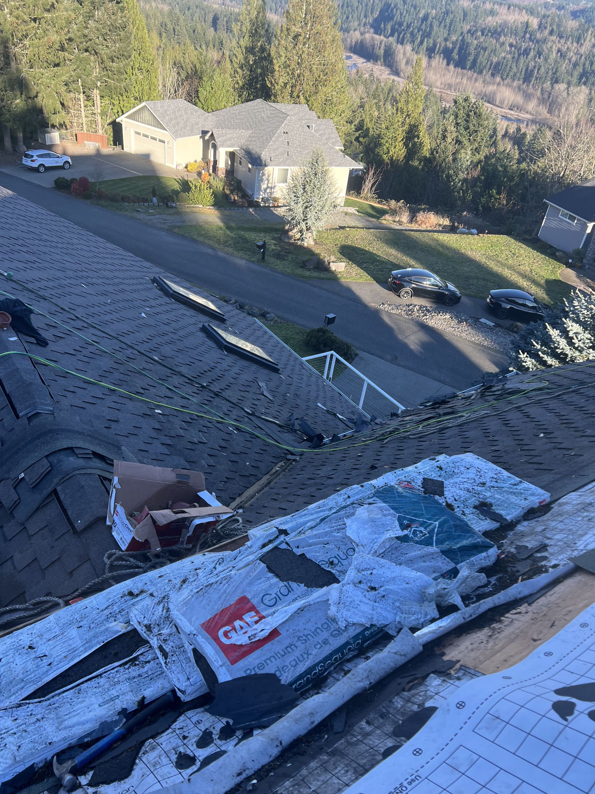 A partially shingled roof with a street and houses in the background. Green trees and a cloudy sky in Bonney Lake, WA.