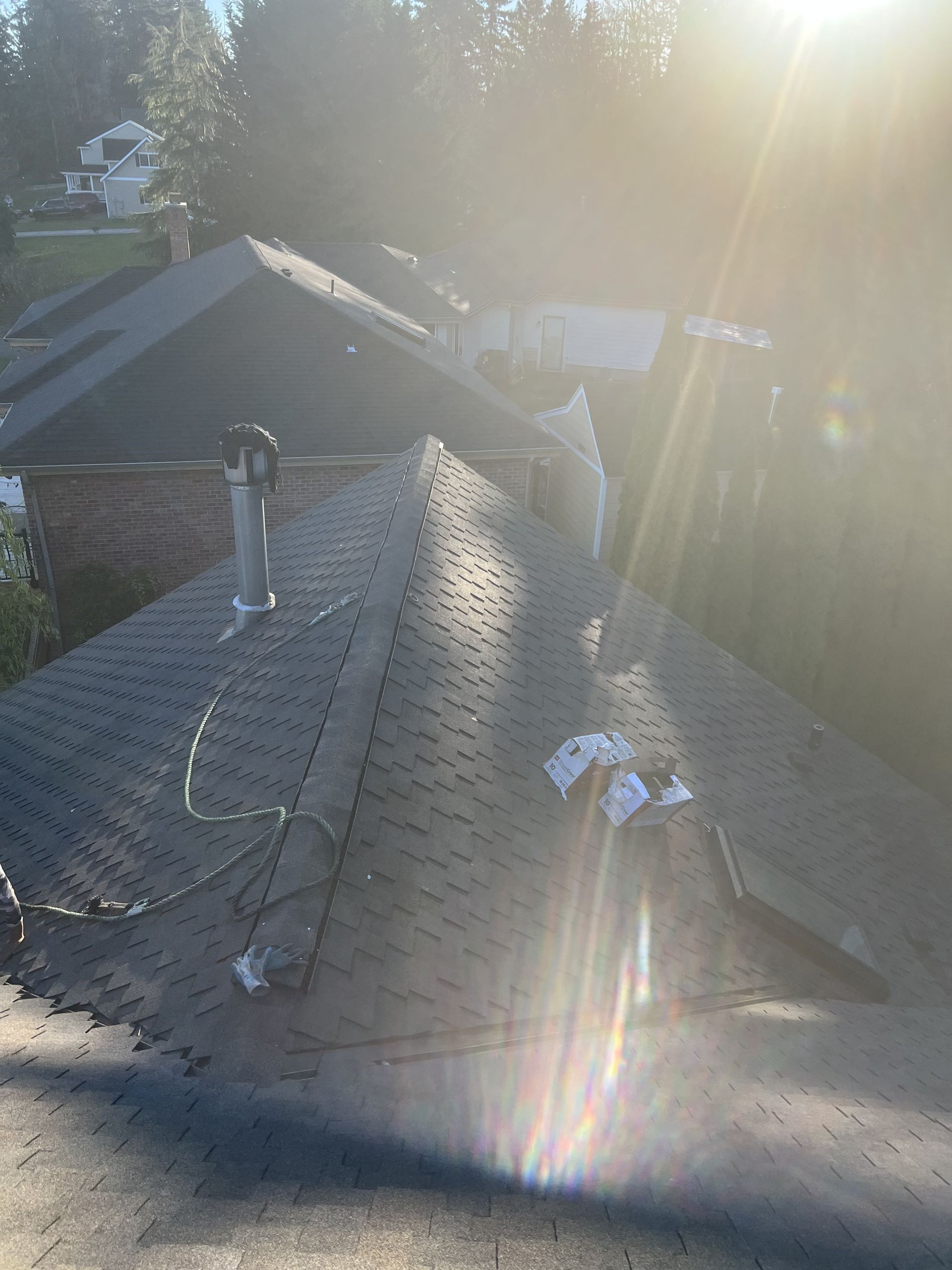 Roof of a house with dark shingles, chimney, and sun glare by Team Roofing NW in Bonney Lake, WA.