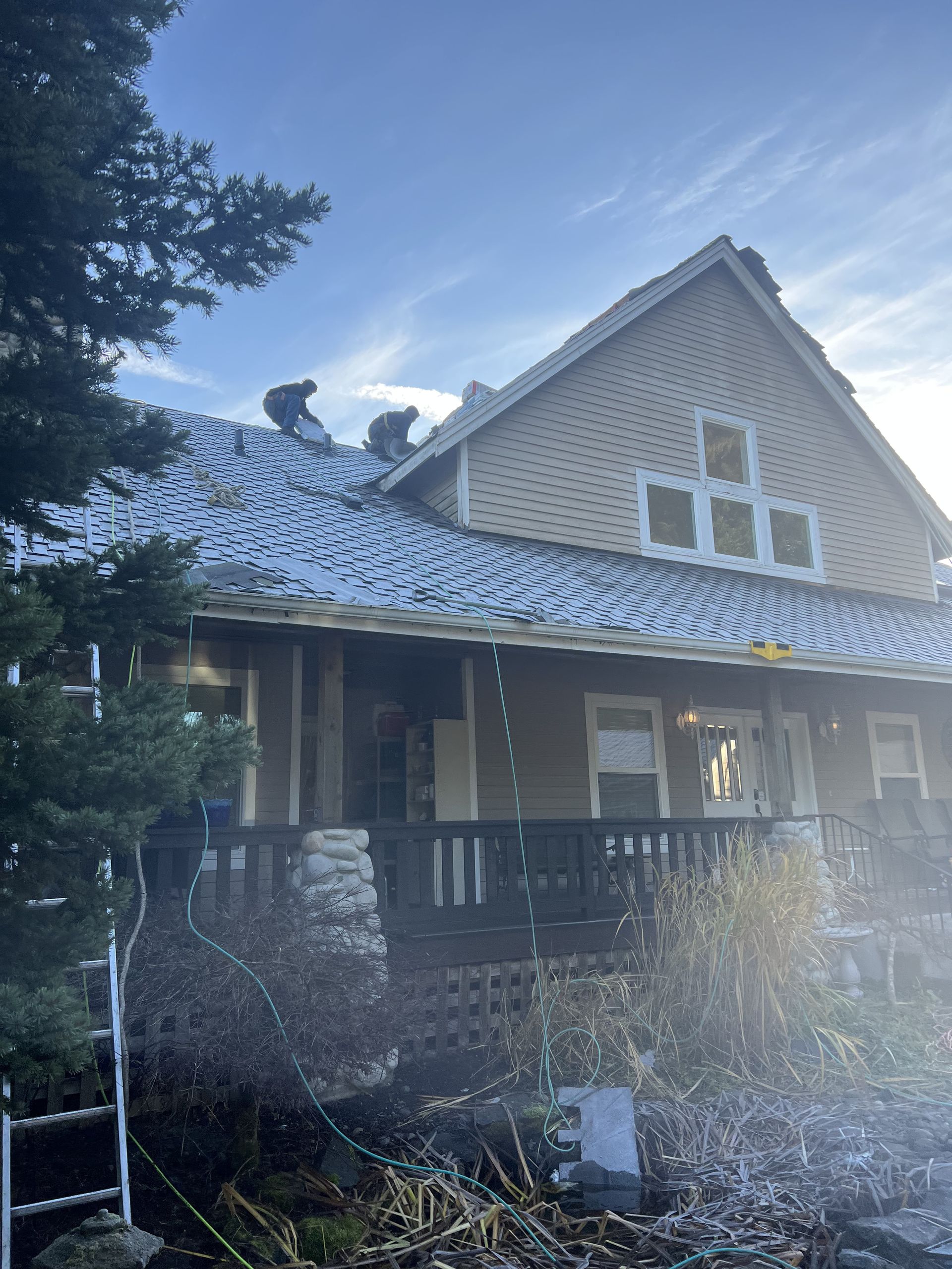 Two people clearing snow from a residential roof. House with porch, snow-covered roof, sunny day by in Bonney Lake, WA.