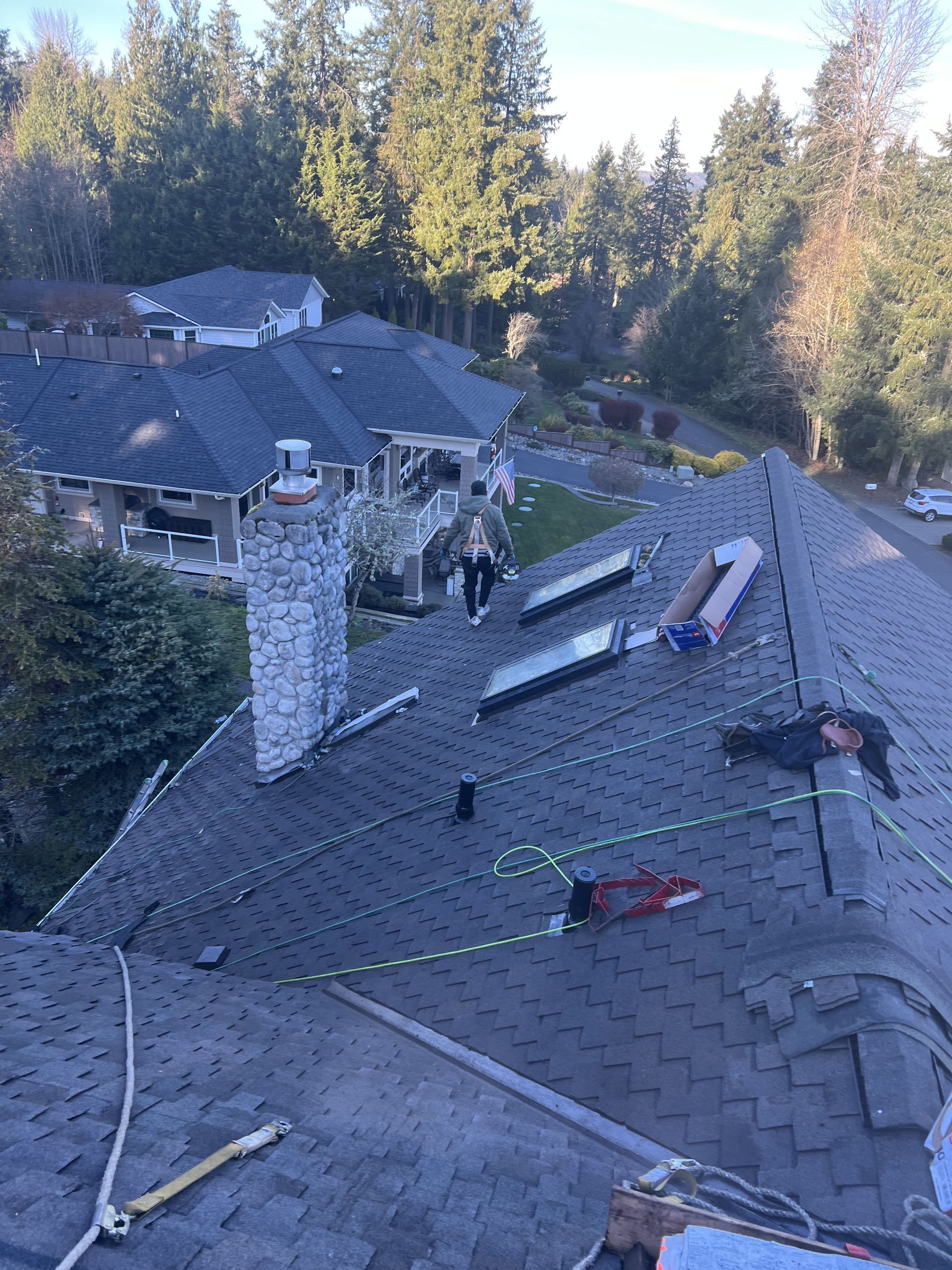 Roofers working on a dark gray shingle roof with skylights, with green safety ropes. by Team Roofing NW in Bonney Lake, WA.