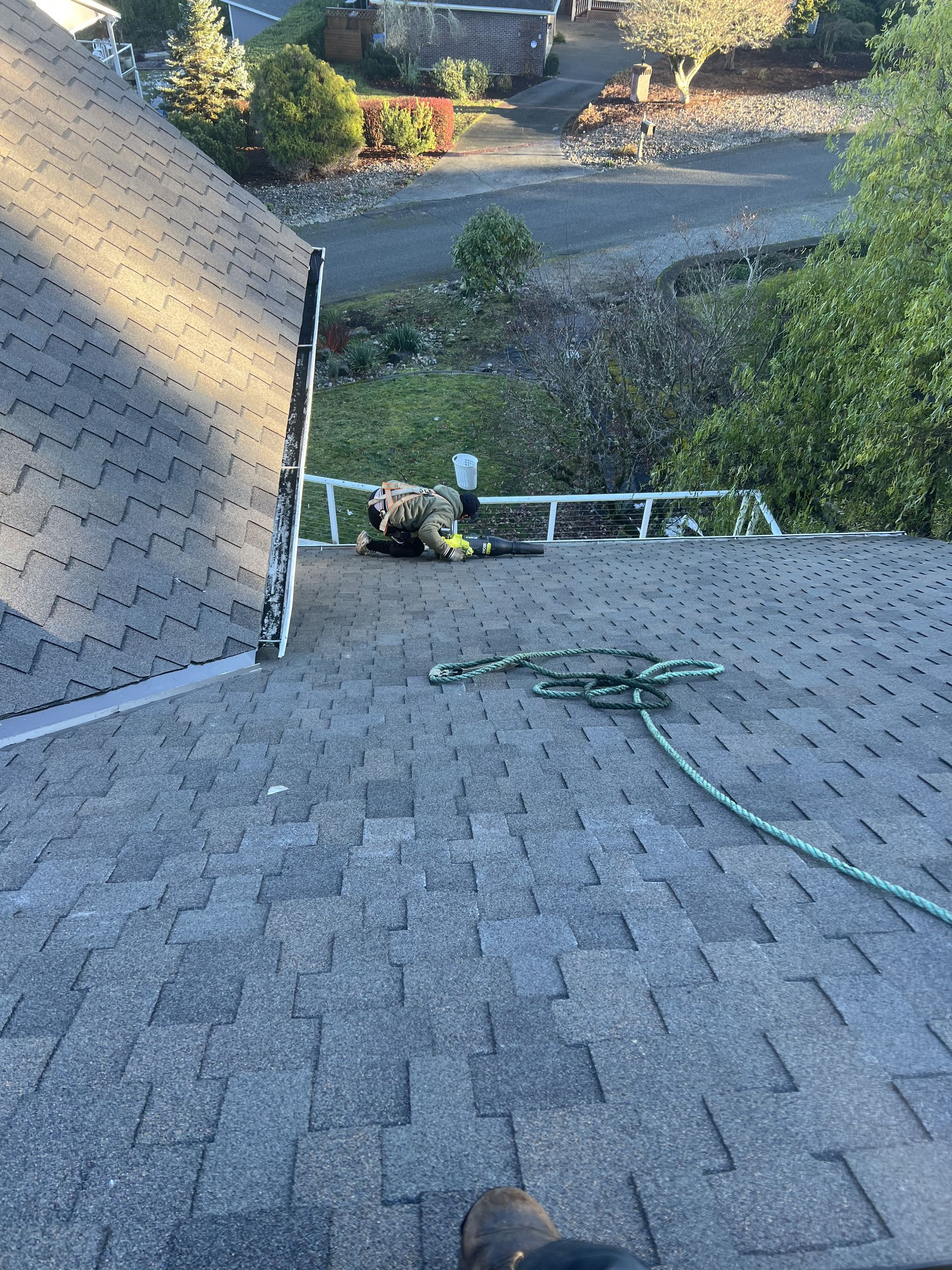 Roofer on a shingled roof, next to a ladder. Green hose and rope on the roof by Team Roofing NW in Bonney Lake, WA.