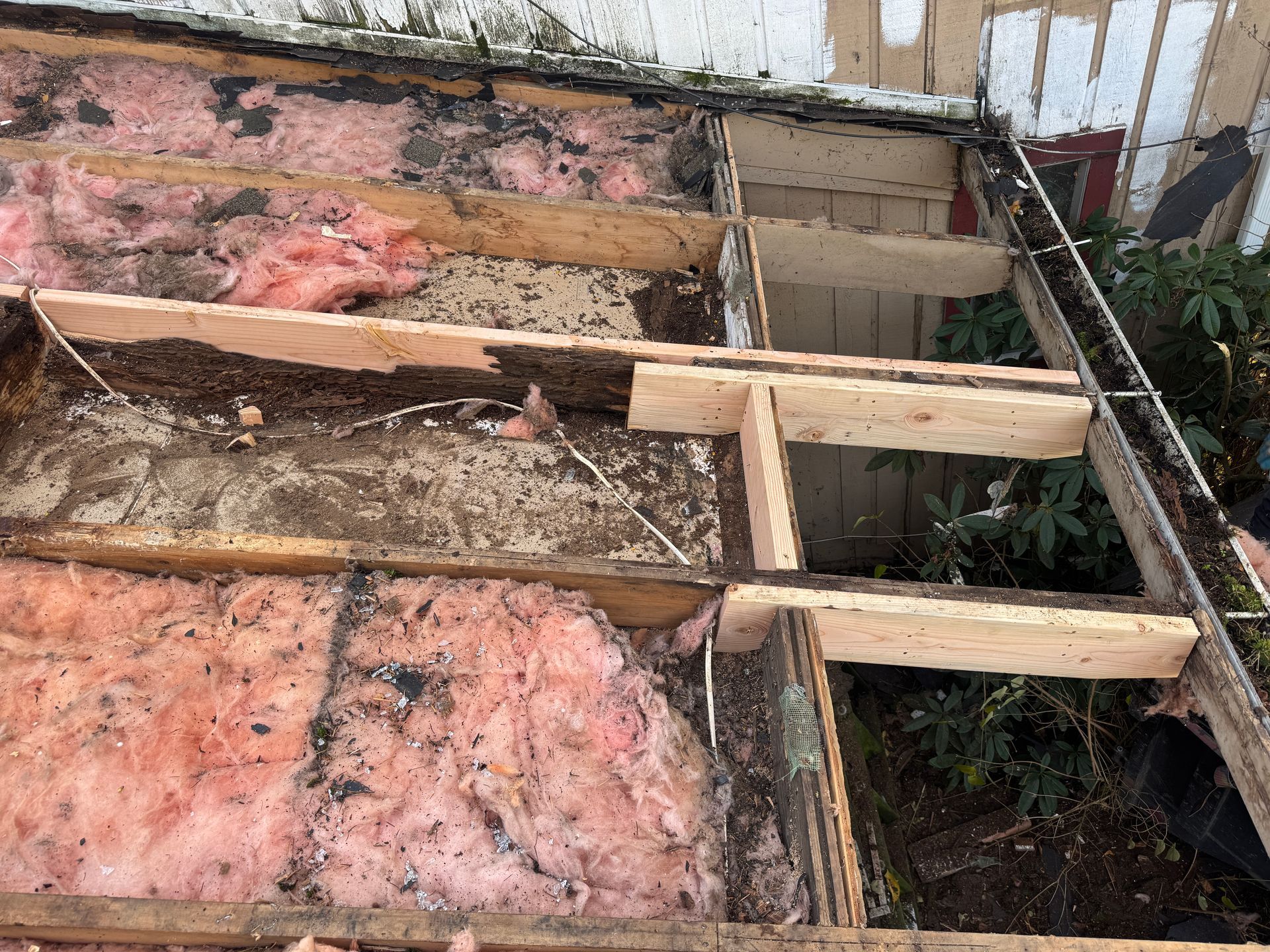 Deconstructed porch floor with exposed wood framing, pink insulation, and debris.