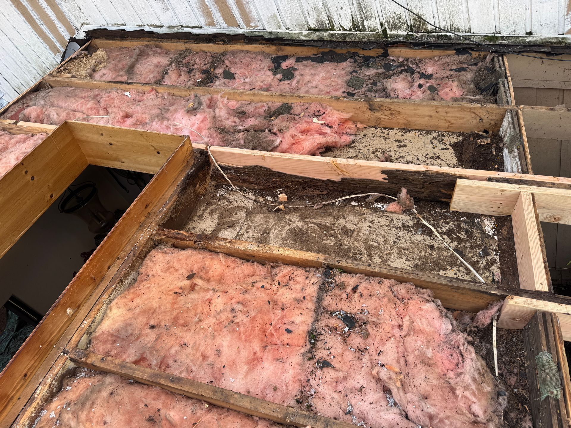 Roof structure under repair, showing exposed wood beams and pink insulation, with signs of water damage and mold.