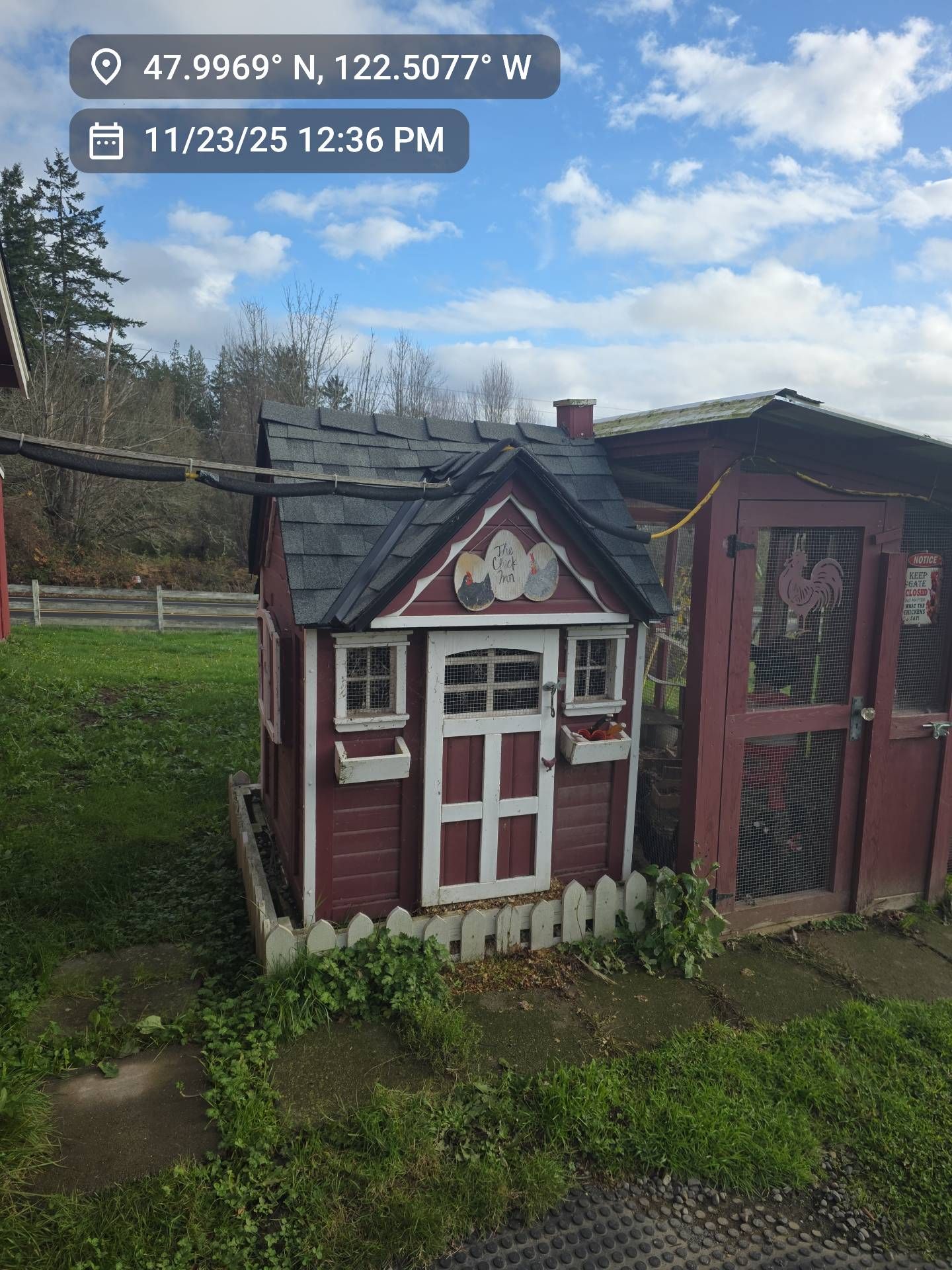 Red and white playhouse with a picket fence on a grassy lawn; next to a chicken coop.