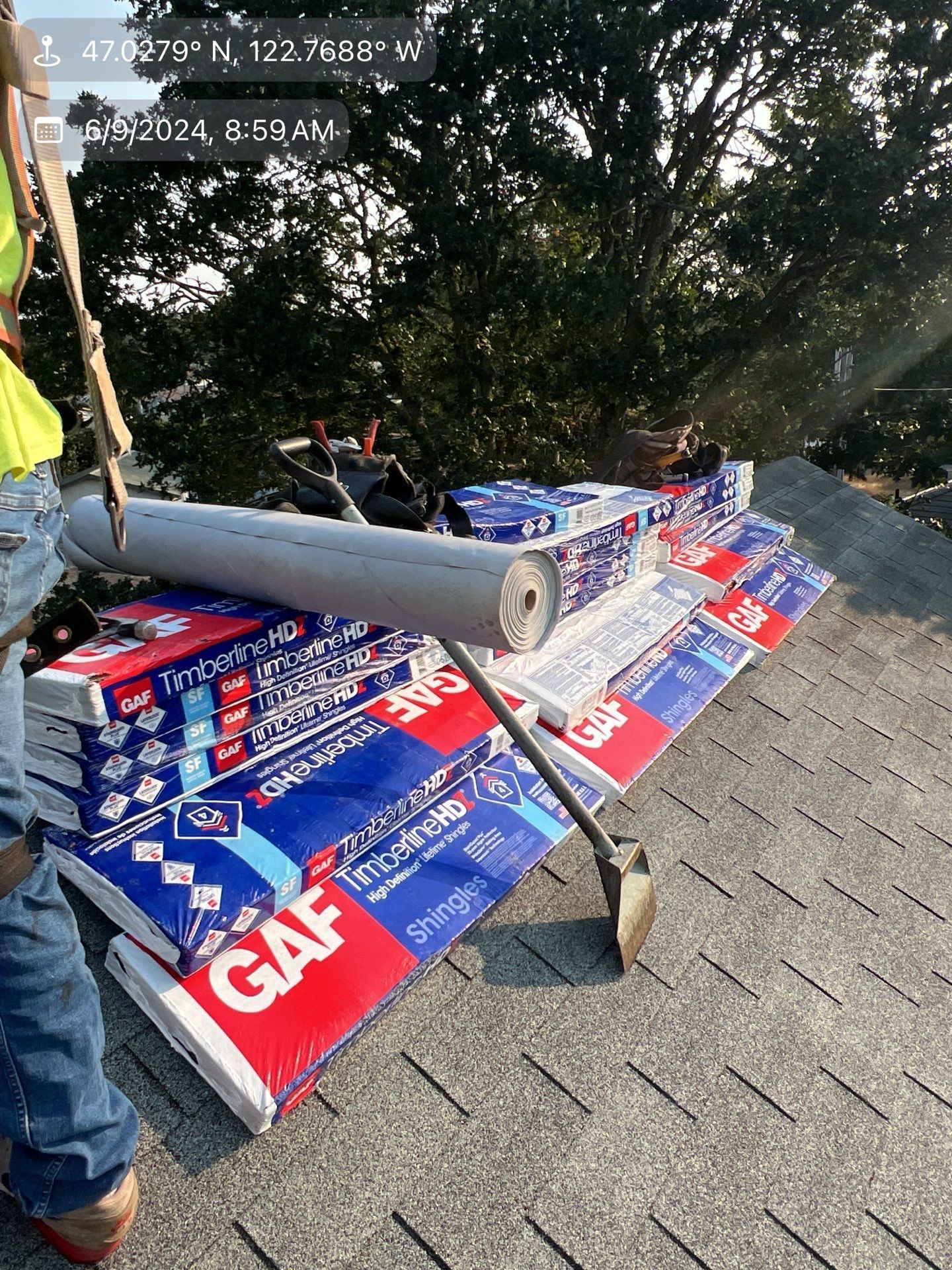 Roofing materials stacked on a rooftop with workers in the background. Packages of GAF shingles