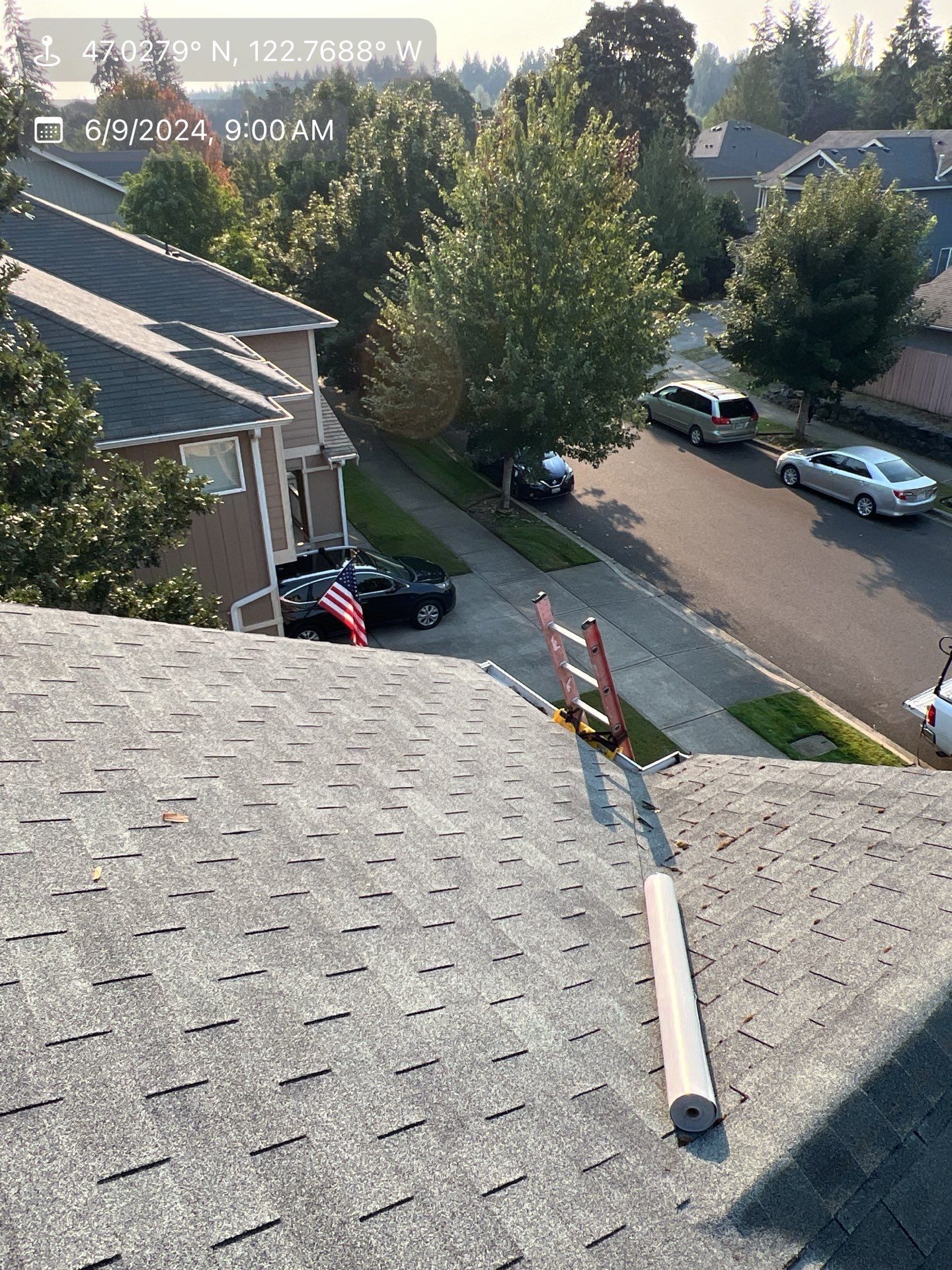 Overhead view of a rooftop with a roll of material. Street with parked cars and houses in the background.