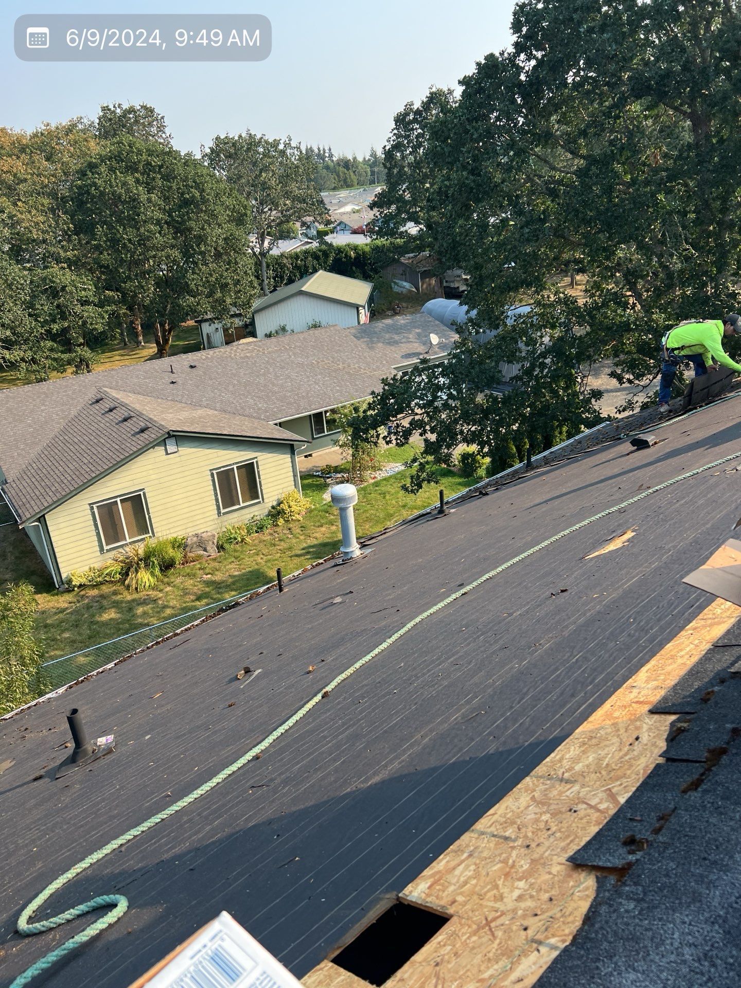 Roofer working on a house roof on a sunny day. Green hose and a white chimney are visible.