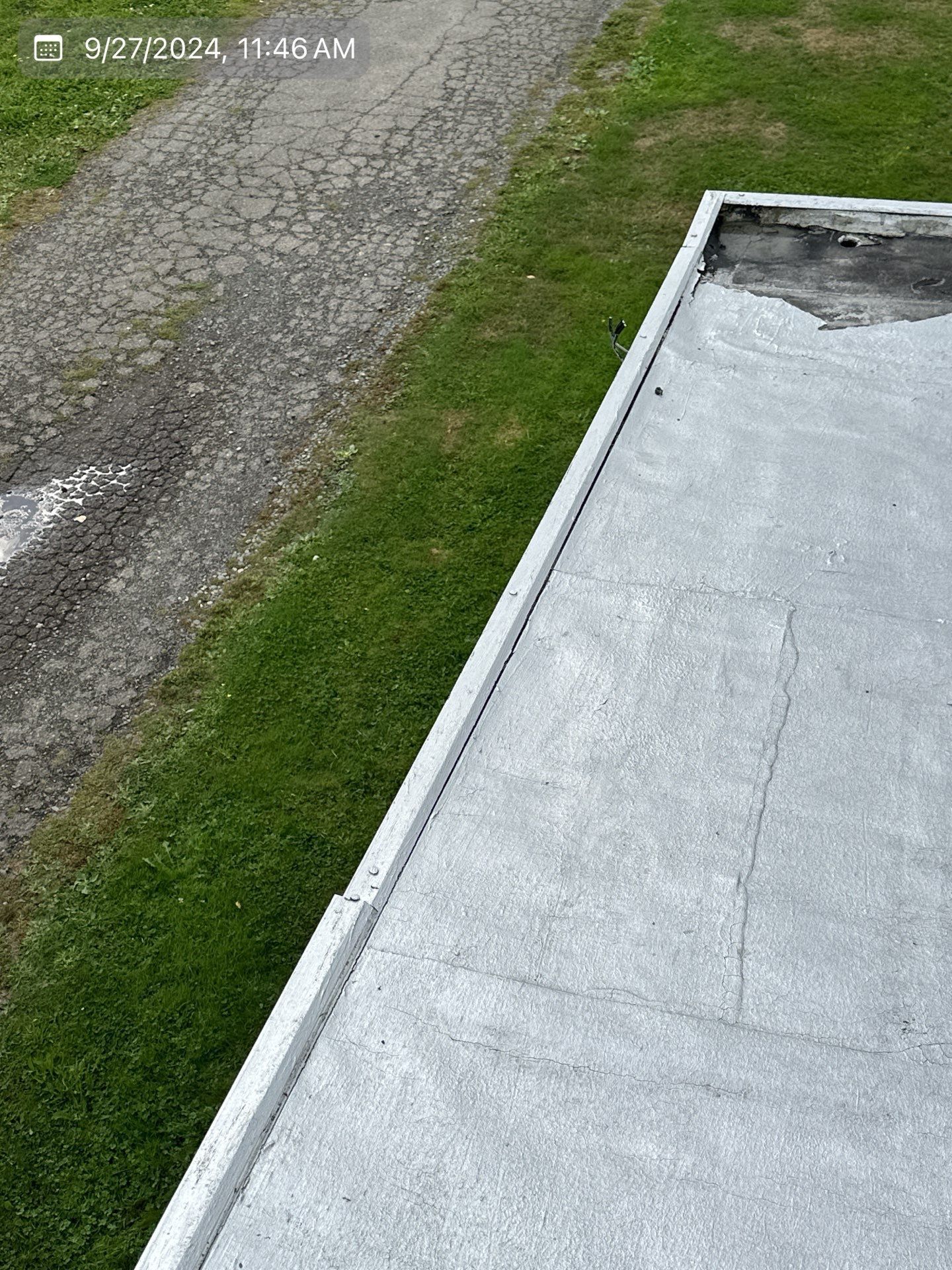 A flat, gray roof edge borders green grass and a gravel driveway.