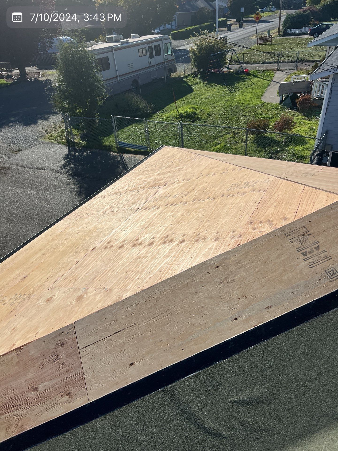 Roof with plywood, on a house, in daylight. Green grass and a road in the background.