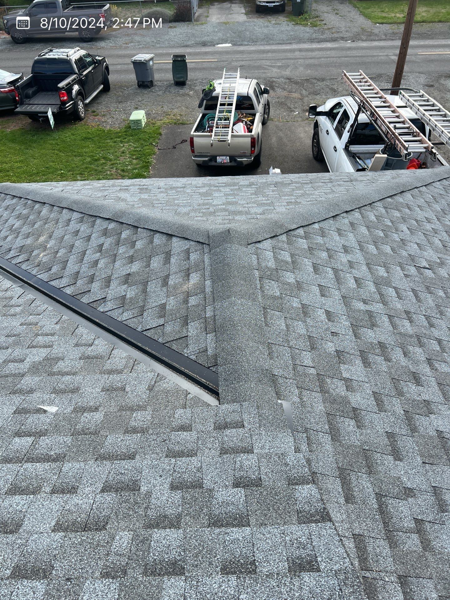 Gray shingled roof with a black metal flashing and a view of several parked trucks in a parking lot.