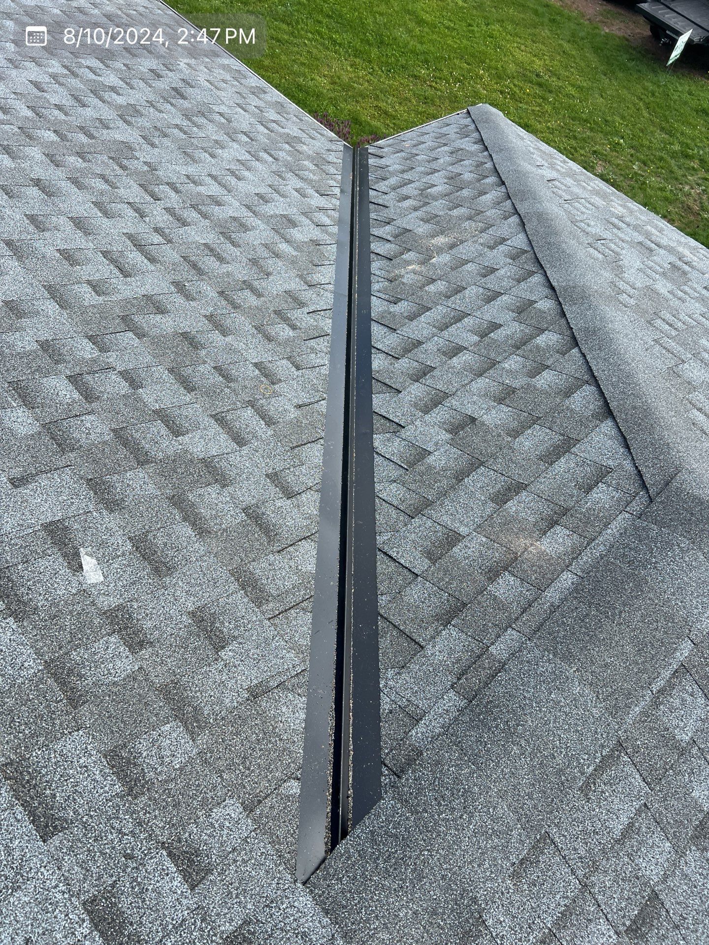Close-up view of a roof peak with gray shingles and a dark metal flashing strip in the middle.
