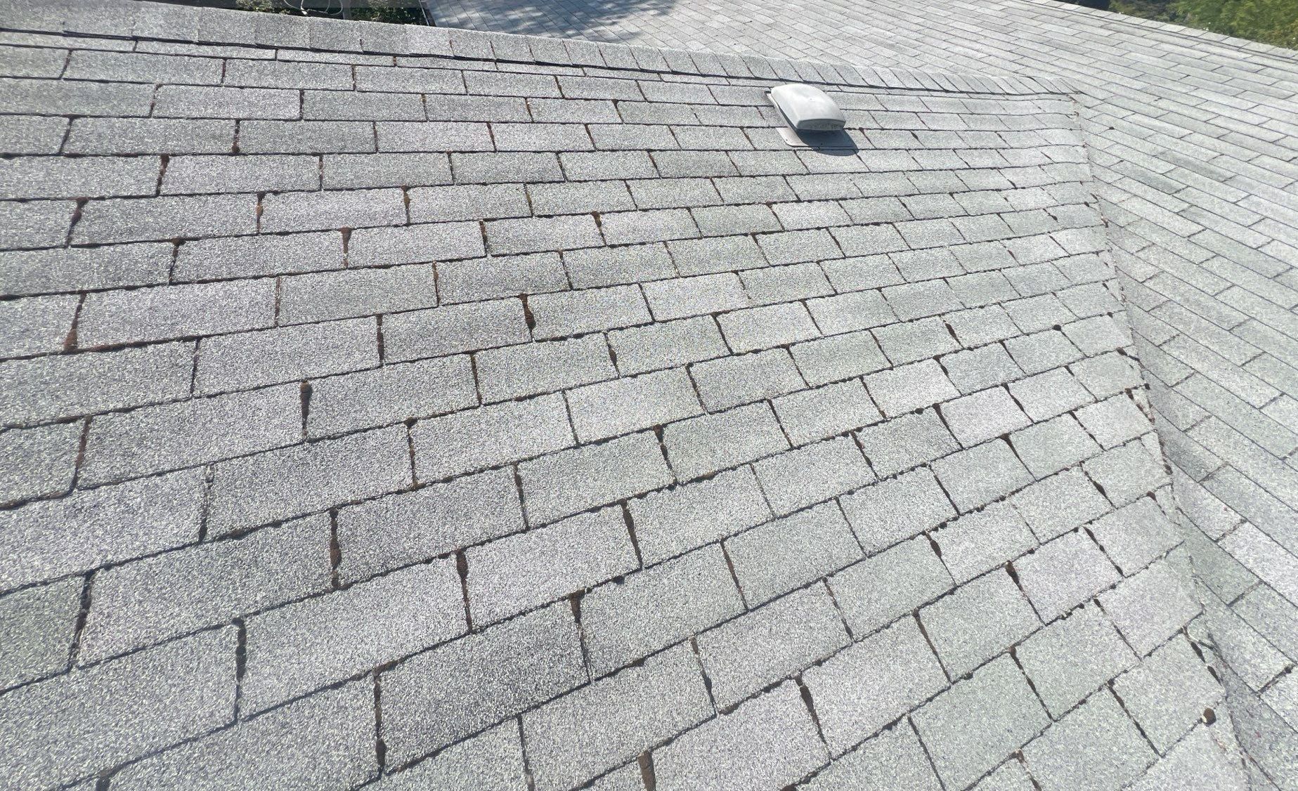 Gray asphalt shingle roof with some wear and a vent in the upper center.
